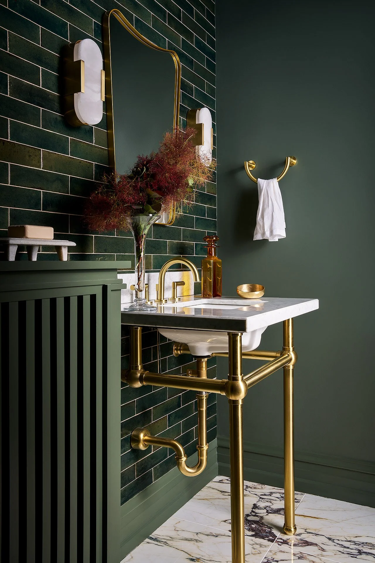 Bathroom with dark green tiled wall, gold fixtures, white marble sink, and marble floor with black and gold veins.