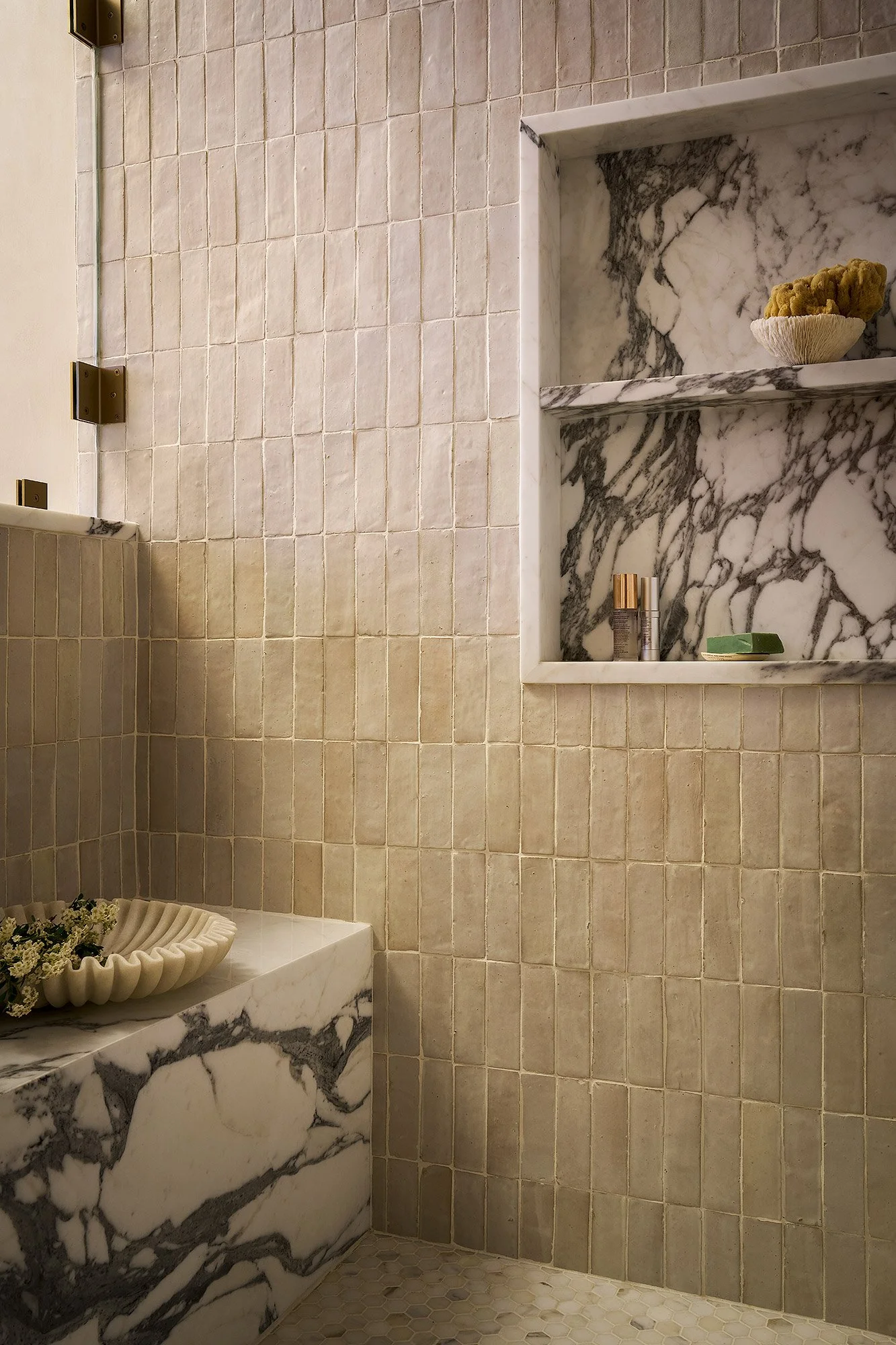 Walk-in shower with zellige tile, integrated marble bench, and custom niche detail.