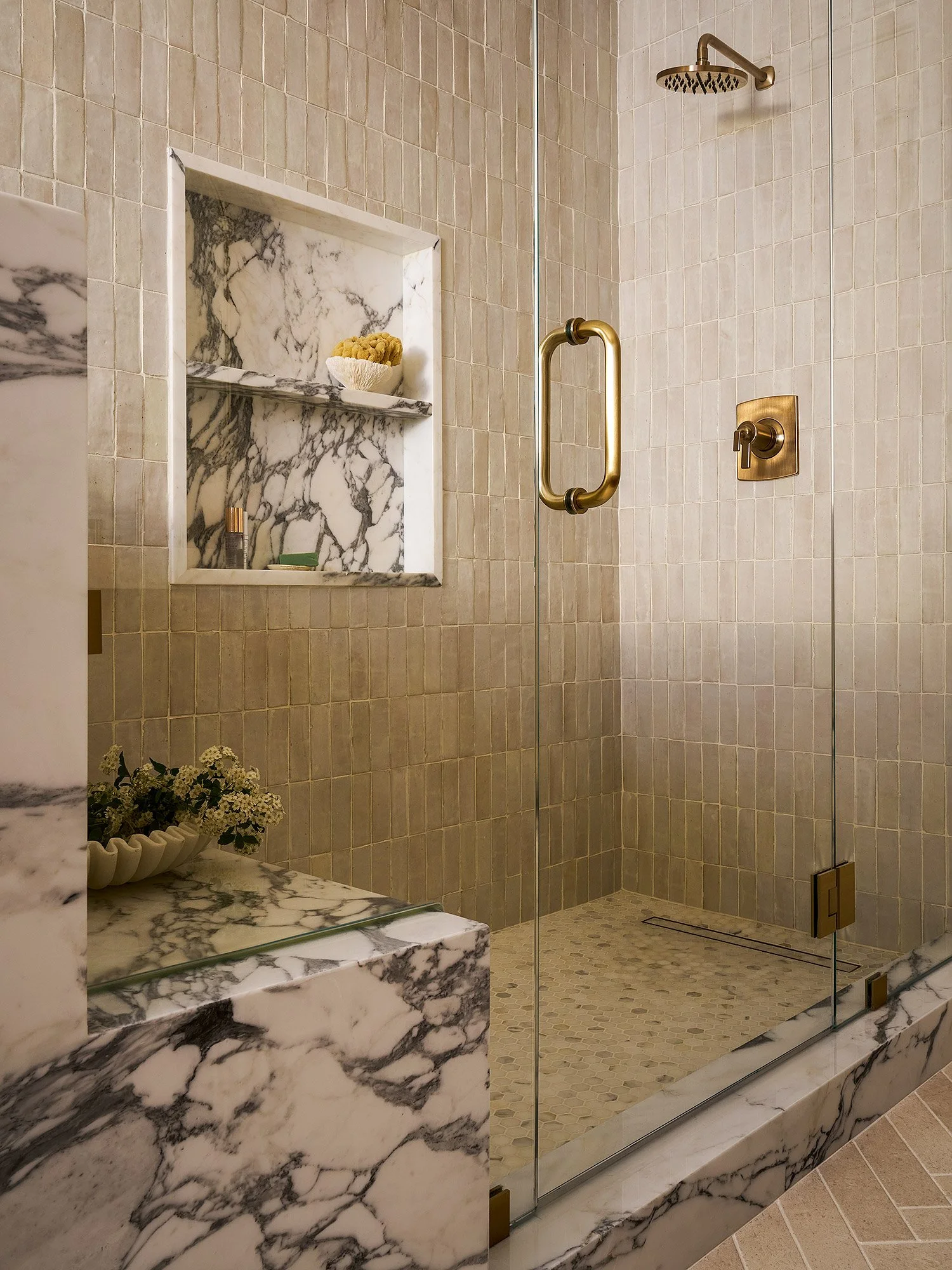 Walk-in shower with zellige tile, integrated marble bench, and custom niche detail.