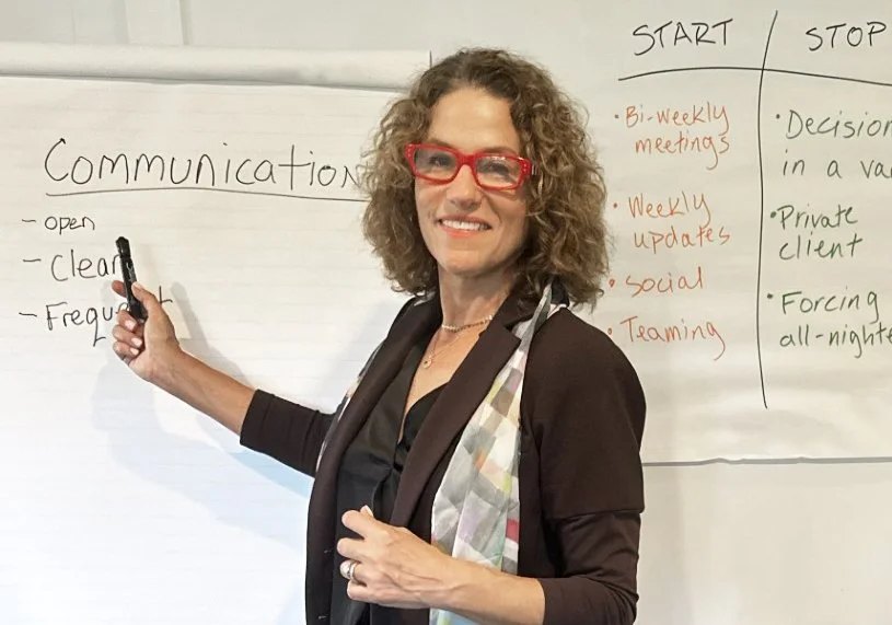 Tammy jersey standing in front of a whiteboard with handwritten notes about communication and leadership coaching.