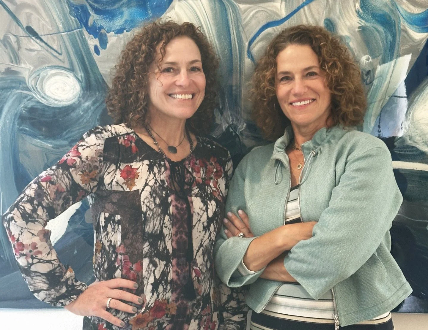 Team optimization specialists, Tammy Jersey and Tracy Rose, smiling and standing in front of an abstract blue and white painting.