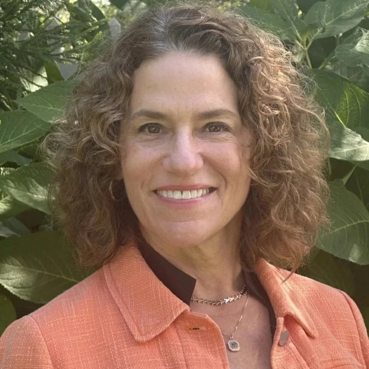 Headshot of Tammy Jersey standing outdoors in front of green foliage.