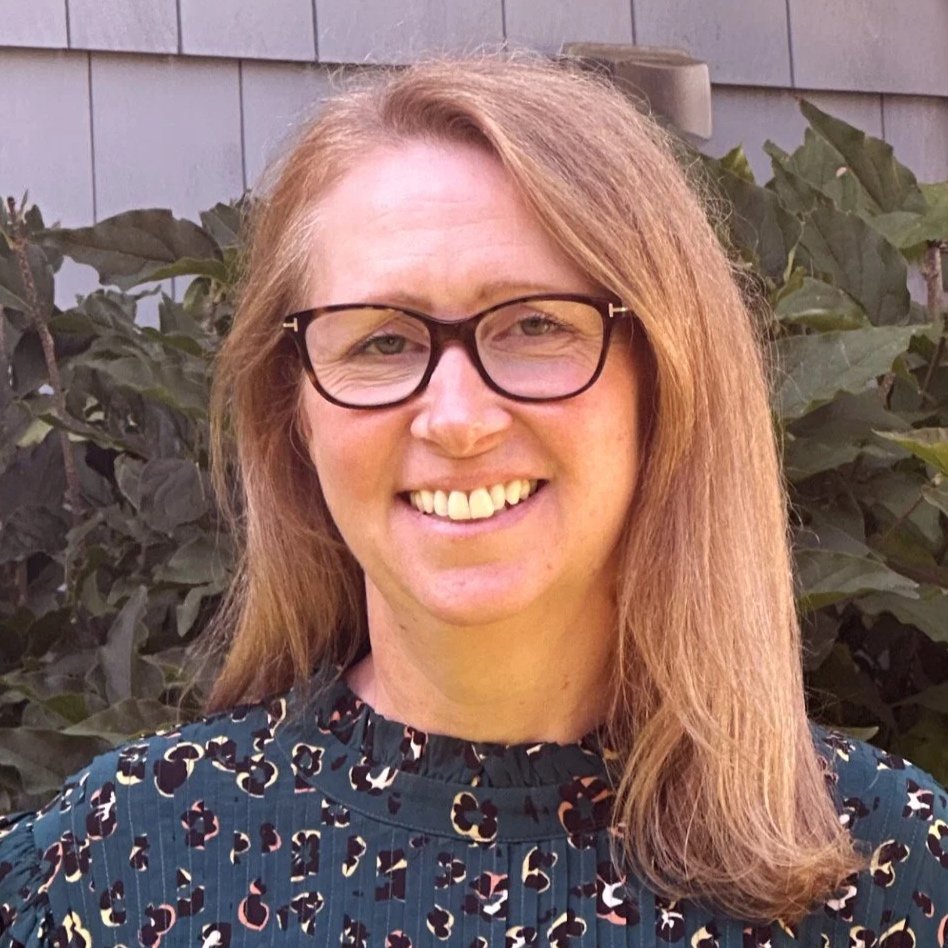Headshot of Chloe Hughes standing outdoors in front of green foliage.