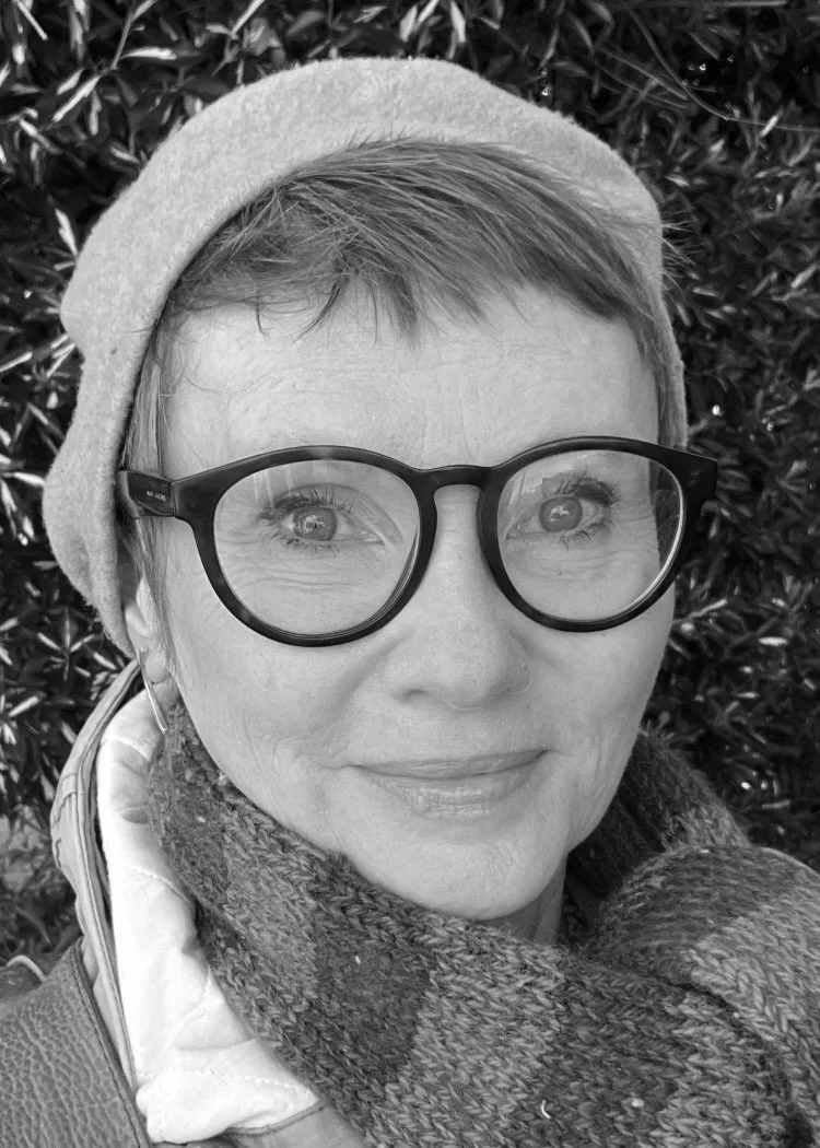 A woman pottery teacher with short hair and glasses wearing a beret and a scarf, smiling, who is great with kids.