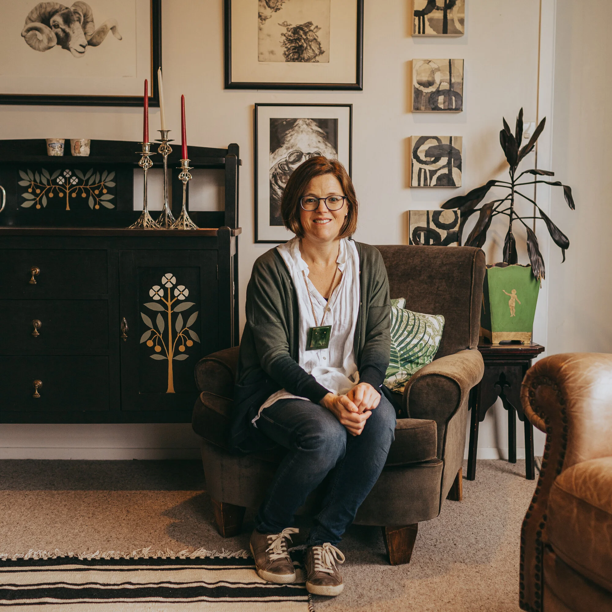Jeanie Simpson sits for the camera in her lovingly curated and designed living room. The cosy, brown lounge chair is the first reupholstery project she ever tackled and is one of her favourite pieces.