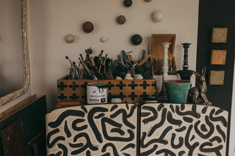 Even Jeanie’s unattached container studio is flamboyant and colourful. The black and white man-robe holds a lot of paint and odds and ends, and is loosely inspired by the work of Keith Haring. The paint brush holder on top is an old school desk Jeanie repurposed and stencilled.
