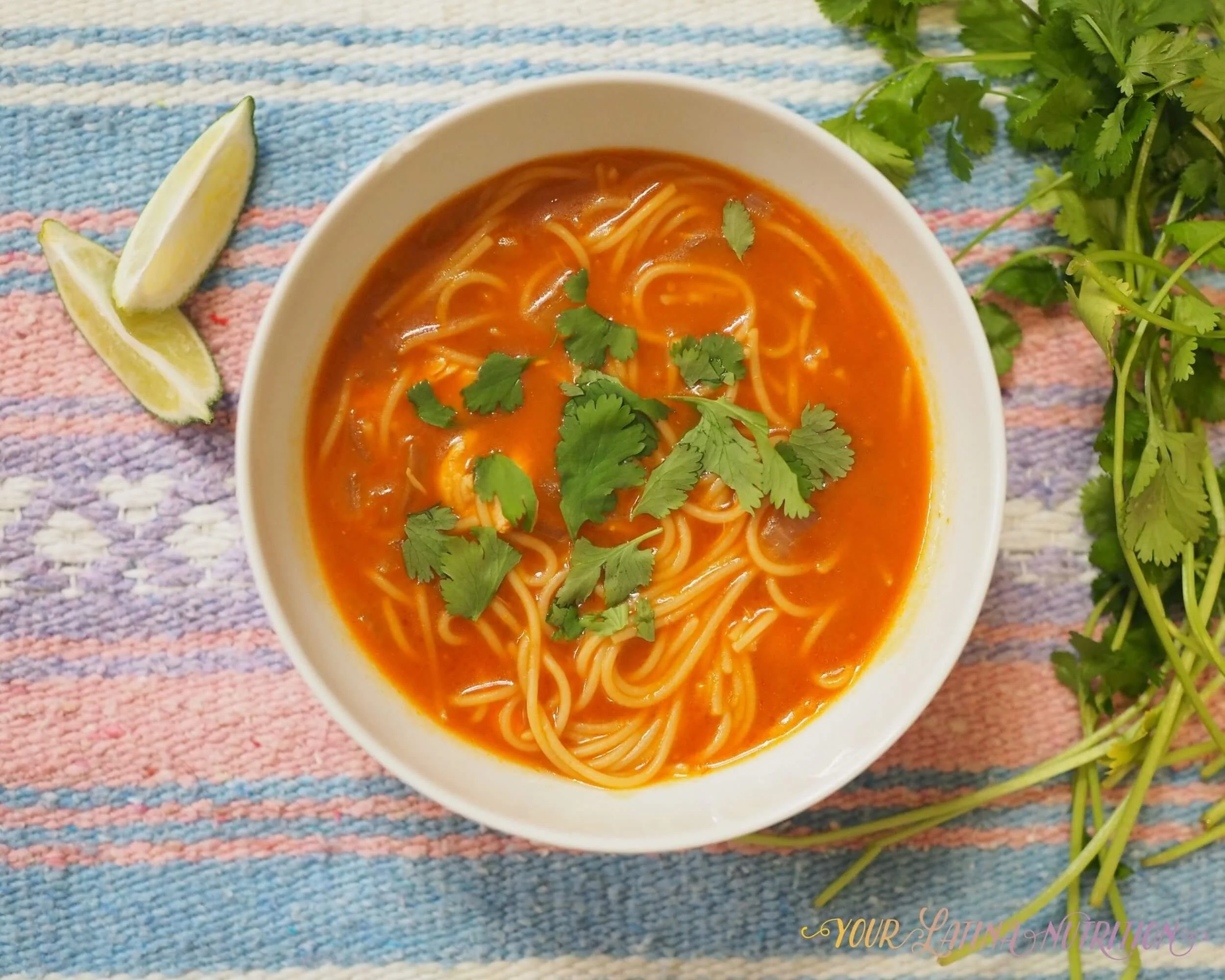 Photo of a bowl of sopa de fideo with lime wedges and cilantro on the side