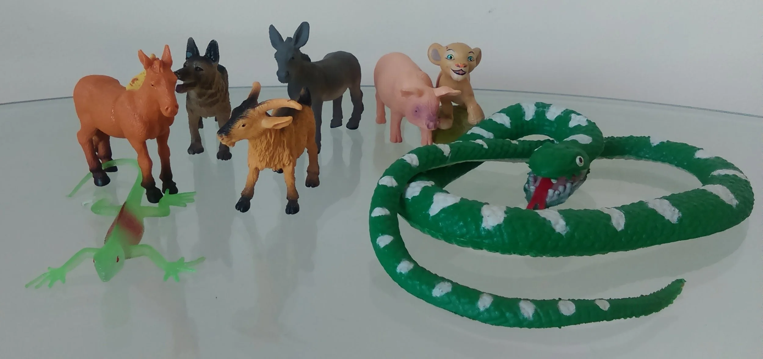 Seven toy animals standing next to a green and white coiled toy snake.