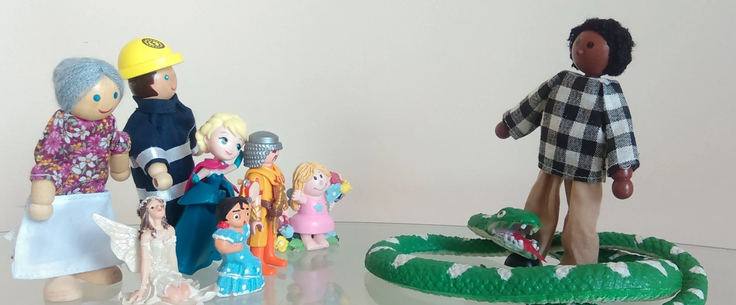 Group of different figurines standing together looking at a doll figurine standing with a green snake coiled around its feet.