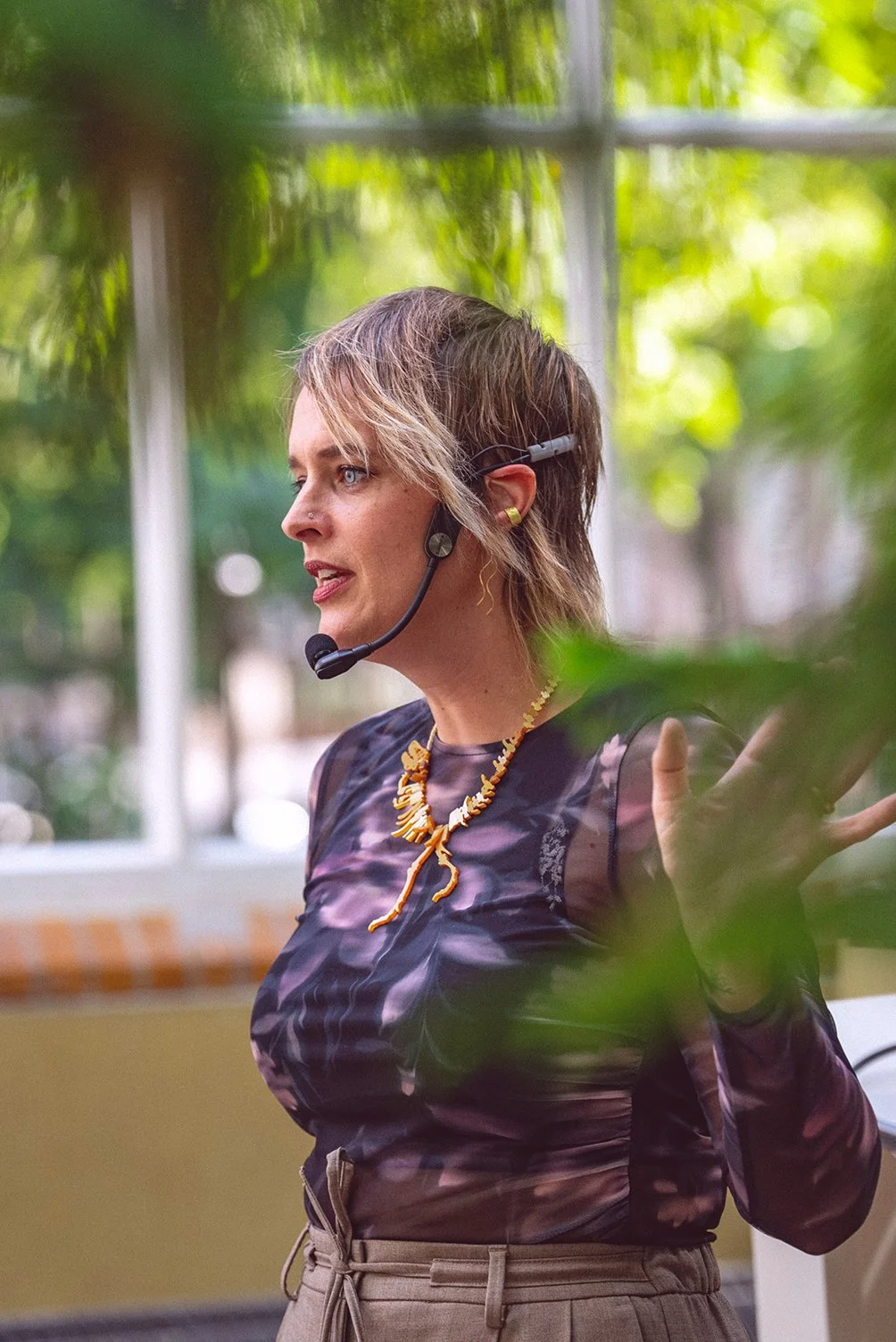 Vrouw met kort haar en een headset, die spreekt en wijst met haar hand, binnen.