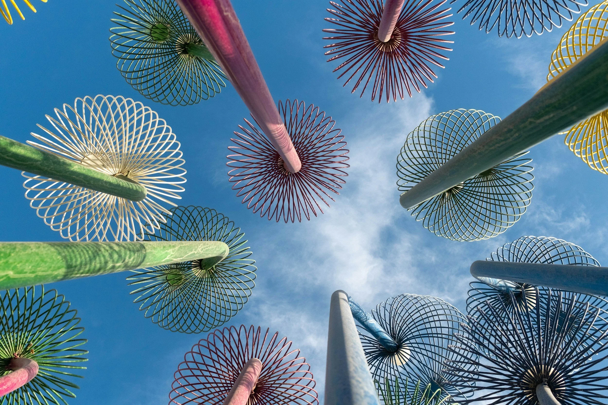 Kleurrijke sierhaken en parasolstokken gezien vanuit beneden tegen een blauwe lucht.