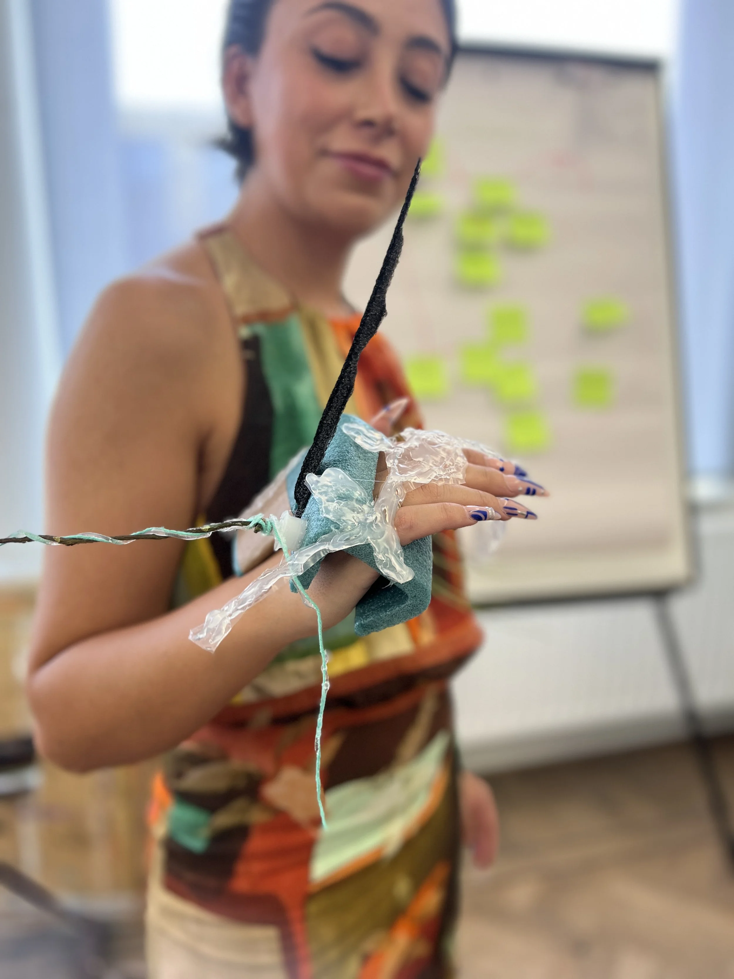 Vrouw met een arm in een zelfgemaakte prosthetische hand, gemaakt van diverse materialen, tijdens een presentatie of workshop in een klaslokaal.