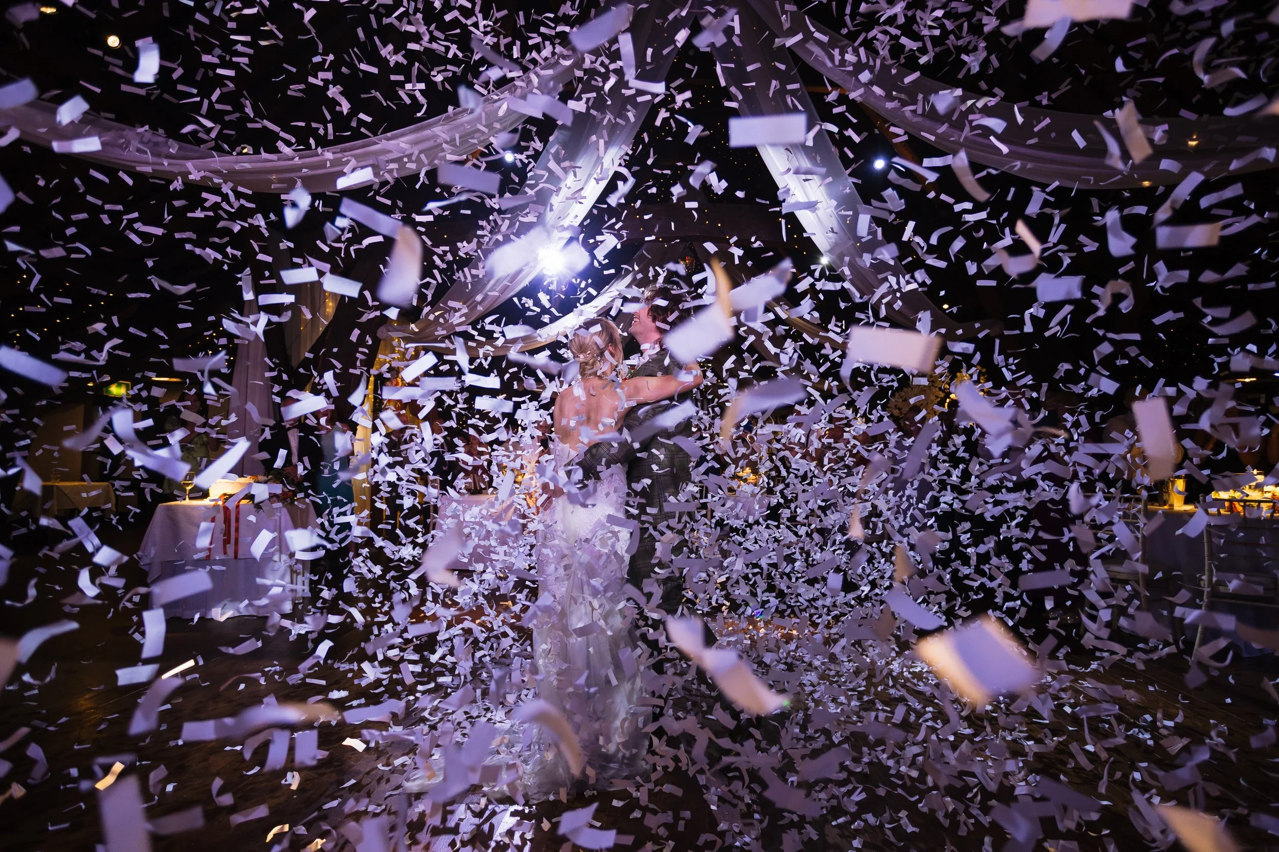 A bride and groom dancing at their wedding reception surrounded by falling confetti.