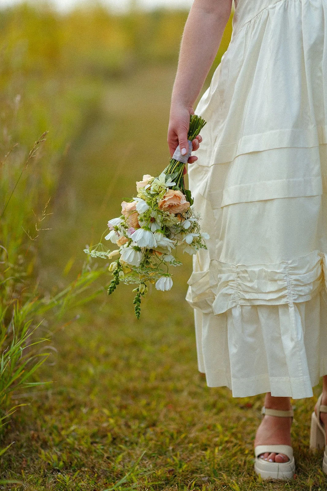 A woman in a white dress holding a bouquet of flowers in a grassy outdoor area.