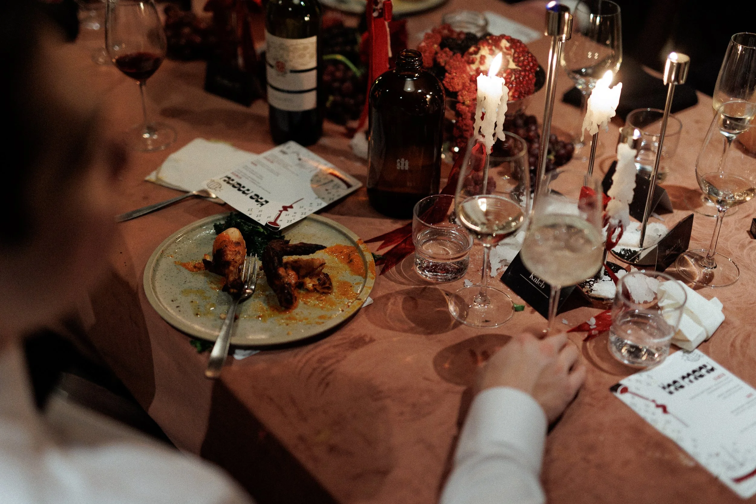 A dinner table with a partially eaten plate of chicken, several glasses of wine, a bottle, lit candles, and festive decorations.