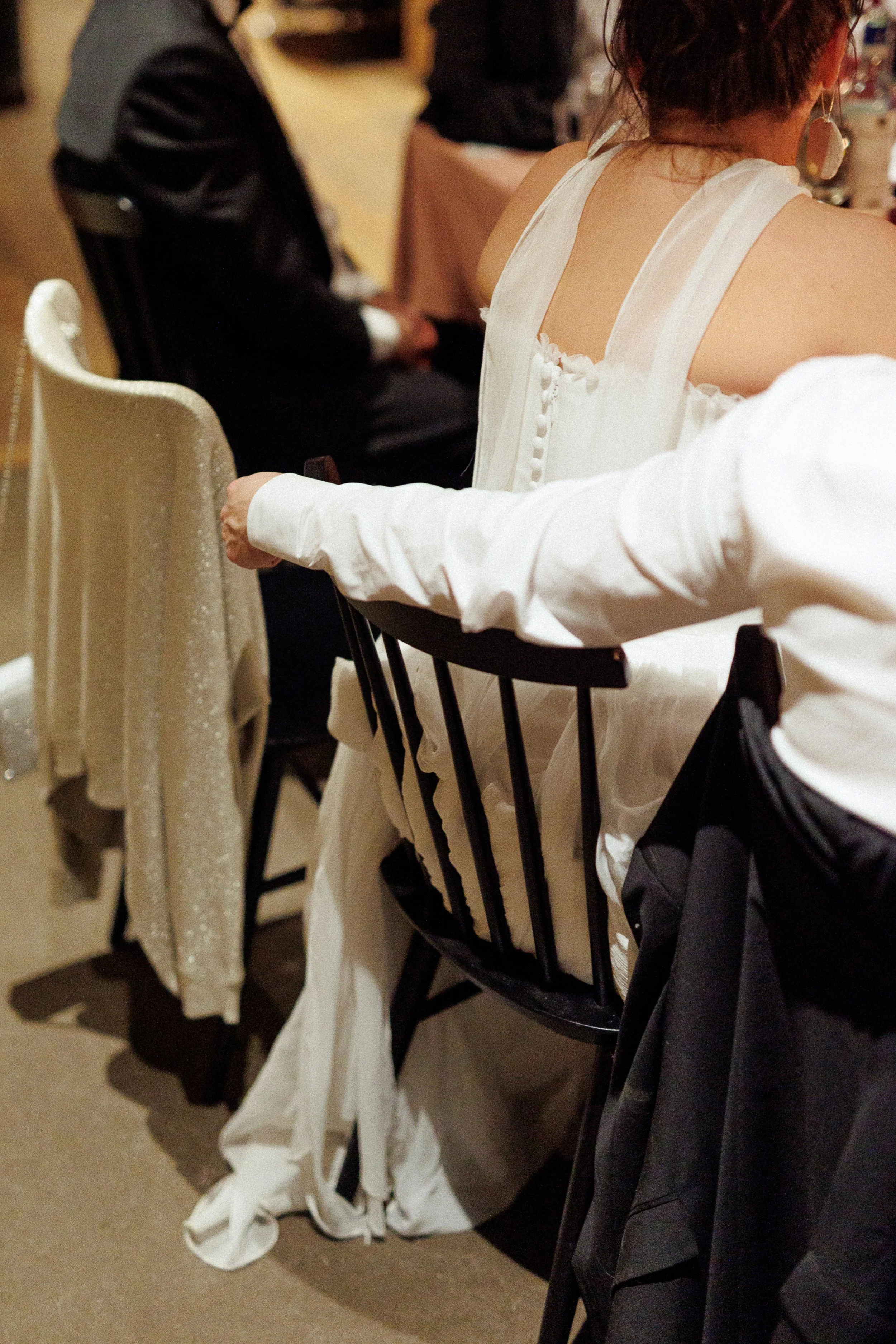 People sitting at a table in formal attire, including a woman in a white dress and a man in a suit, at what appears to be a celebration or event.