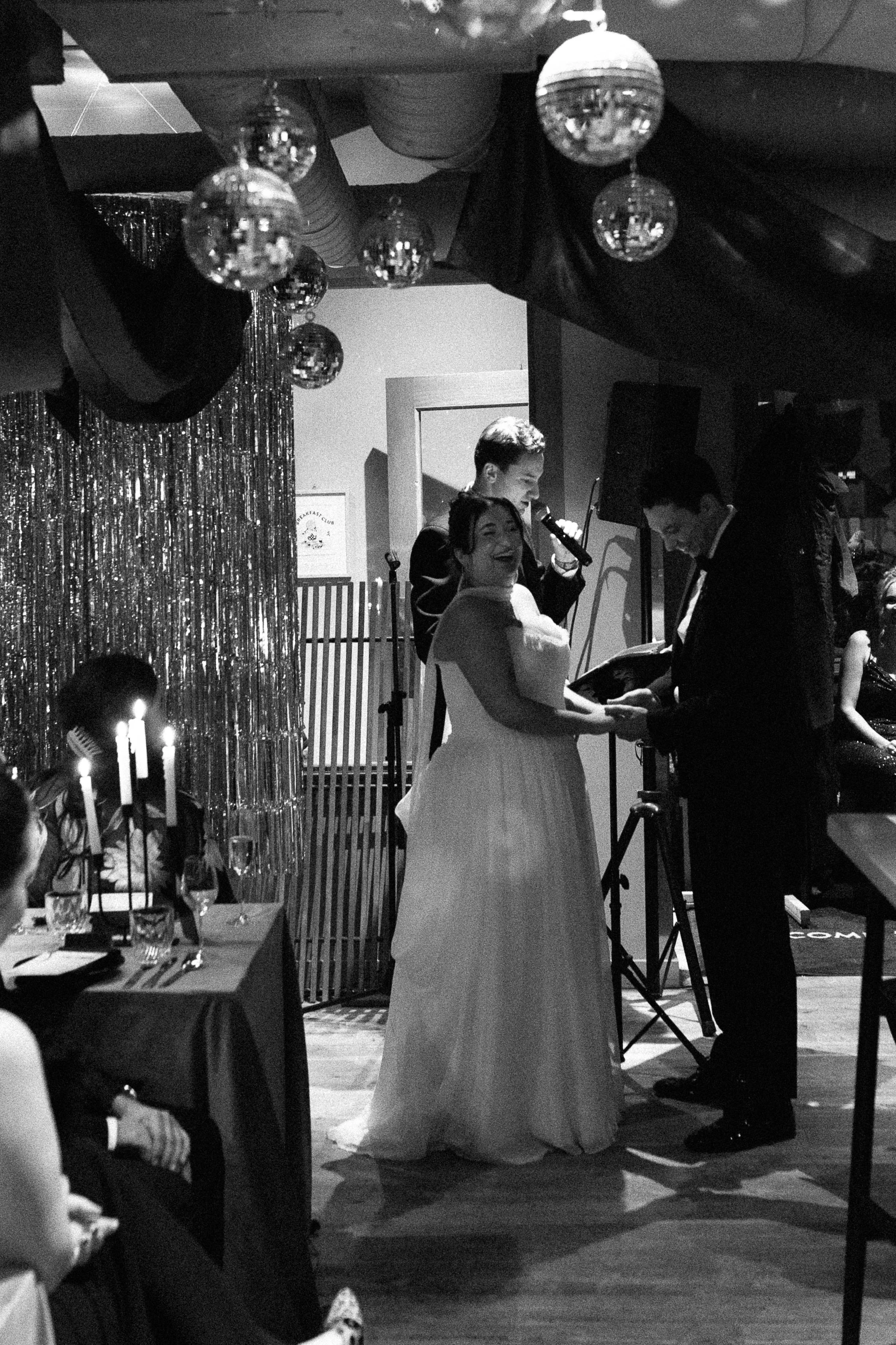 A wedding ceremony where a couple exchanges rings, with a singer performing in the background, surrounded by guests at a decorated venue.