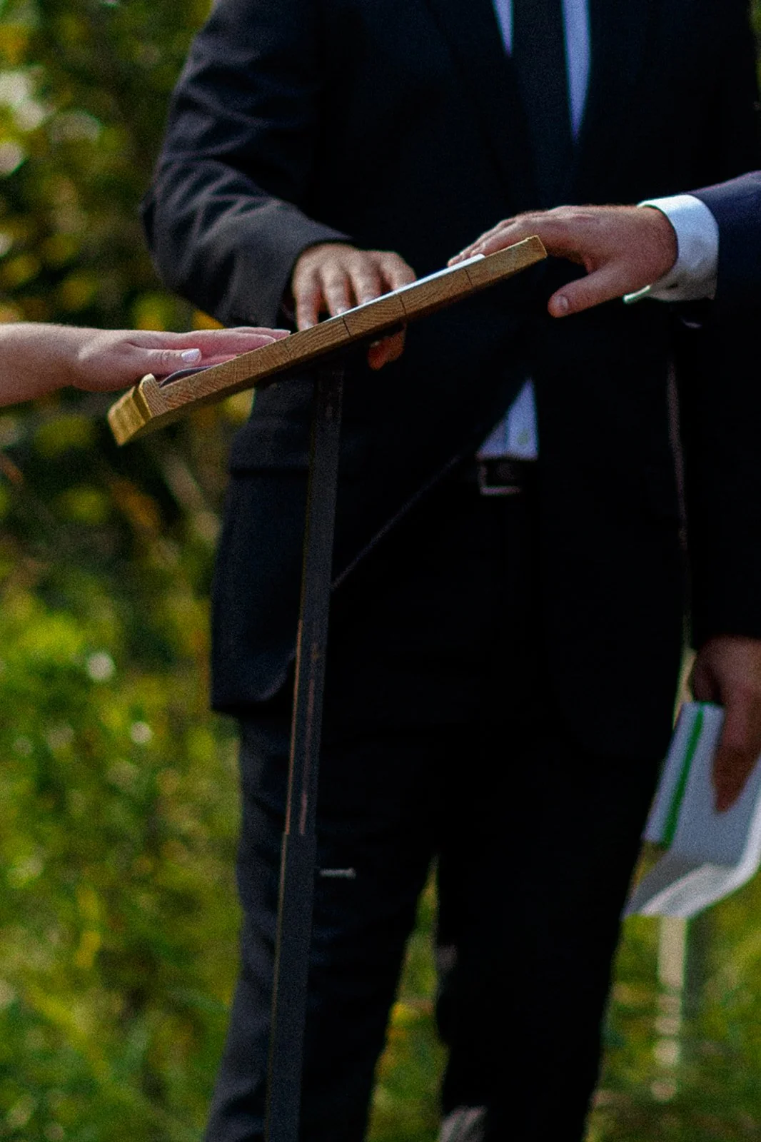 A person in a suit is taking an oath on a wooden platform with their hand on a small book held by another person.
