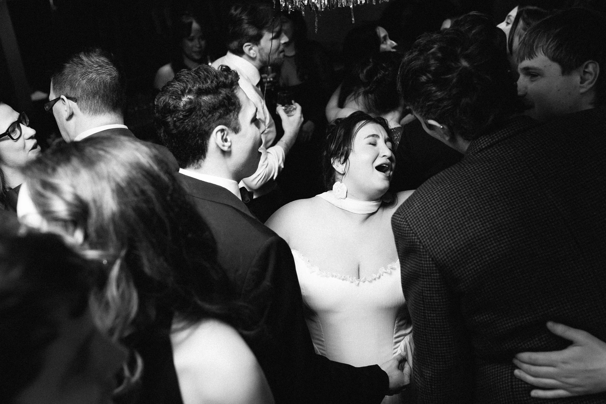 A woman appears to be crying or upset in a crowded scene with multiple people dressed formally, possibly at a party or event, in black and white.