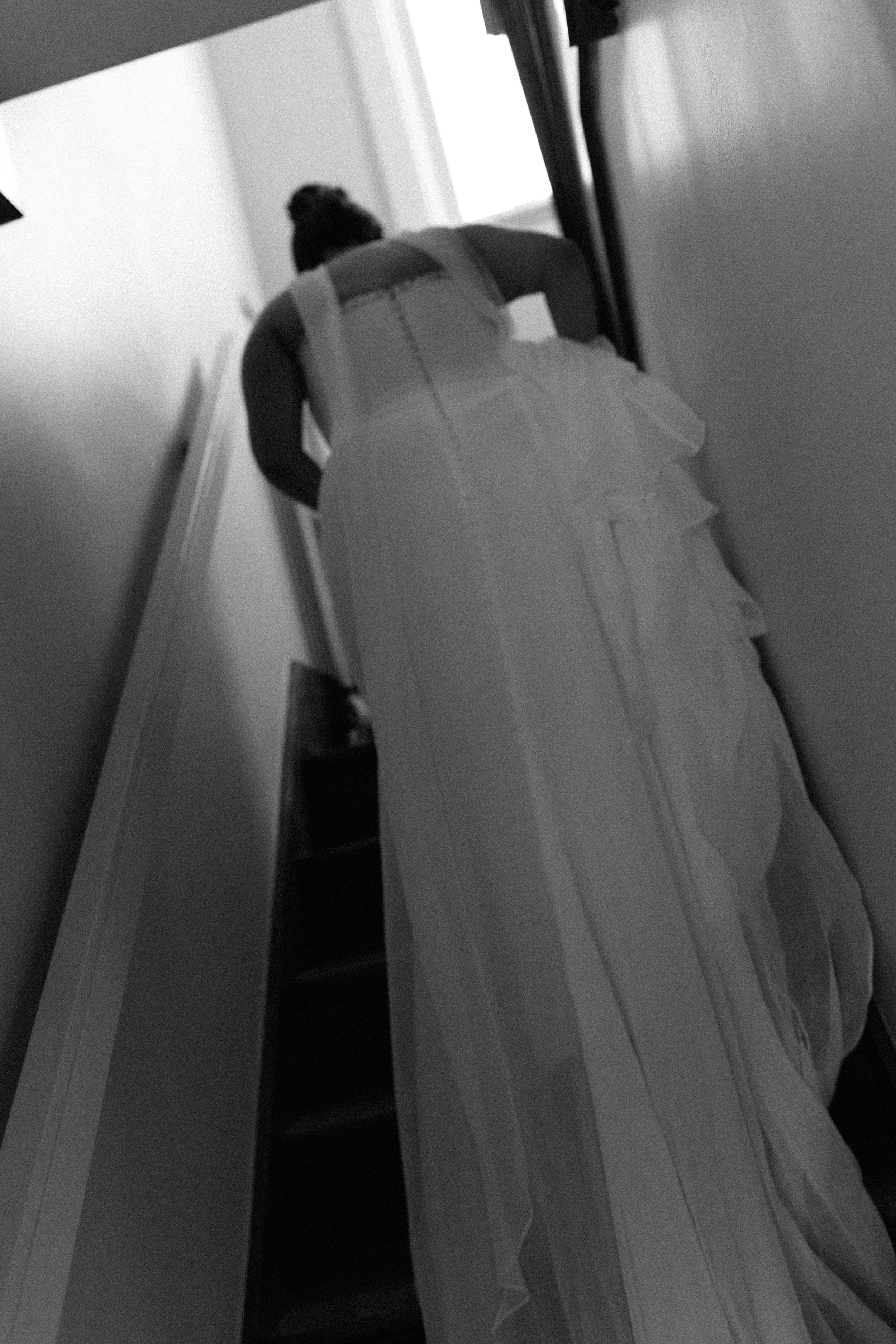 A woman in a wedding dress leaning against a wall in a narrow hallway, viewed from a low angle.
