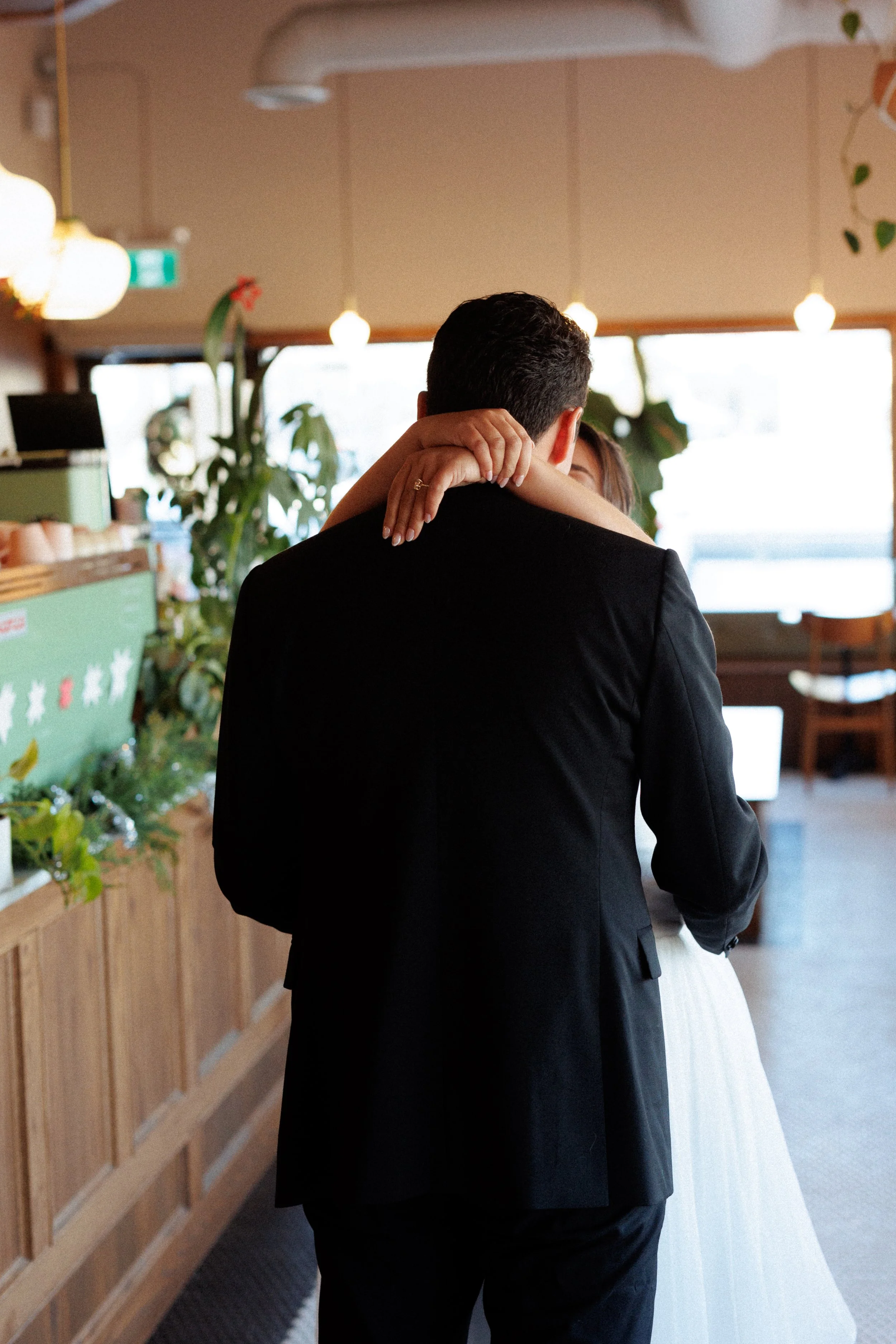 A couple embracing, with the woman’s arms around the man’s neck inside a cozy, warmly lit cafe or restaurant.