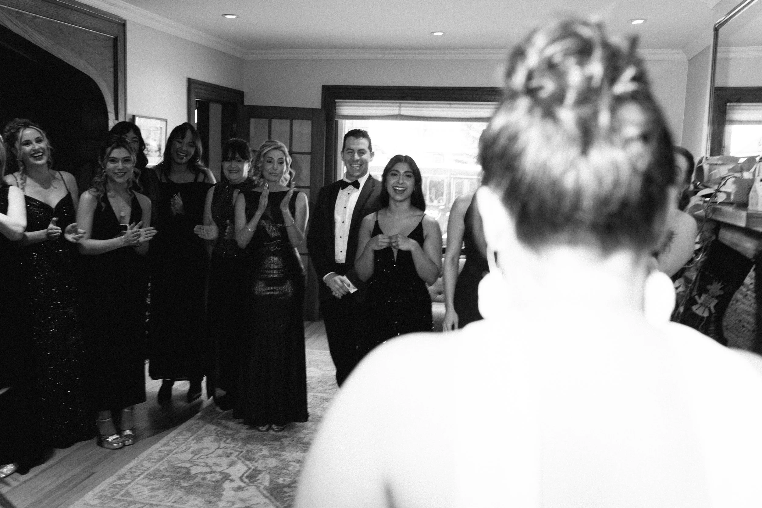 A group of people dressed in formal attire, standing together in a room, with one person in the foreground facing away from the camera.