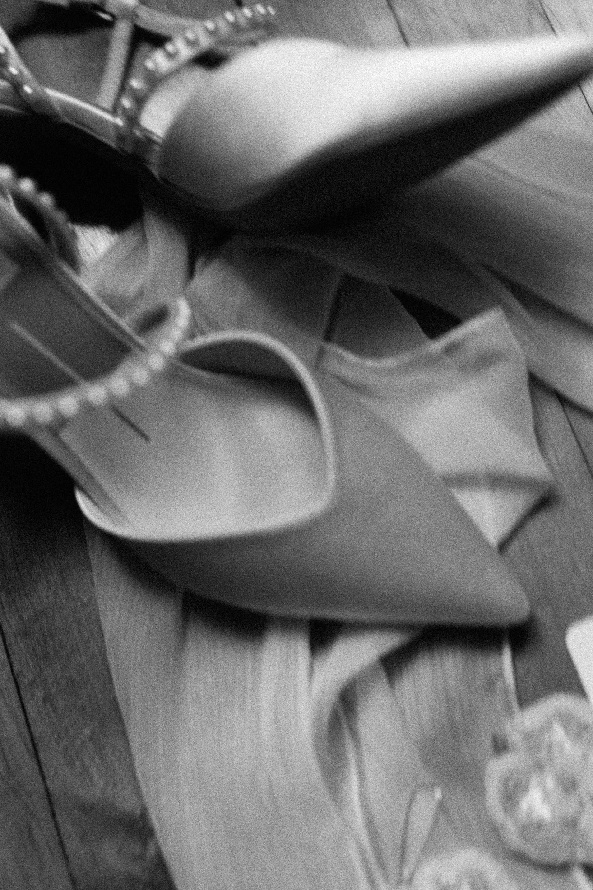 A collection of women's shoes, including high-heeled boots, pointed-toe heels, and sandals, arranged on a wooden floor.