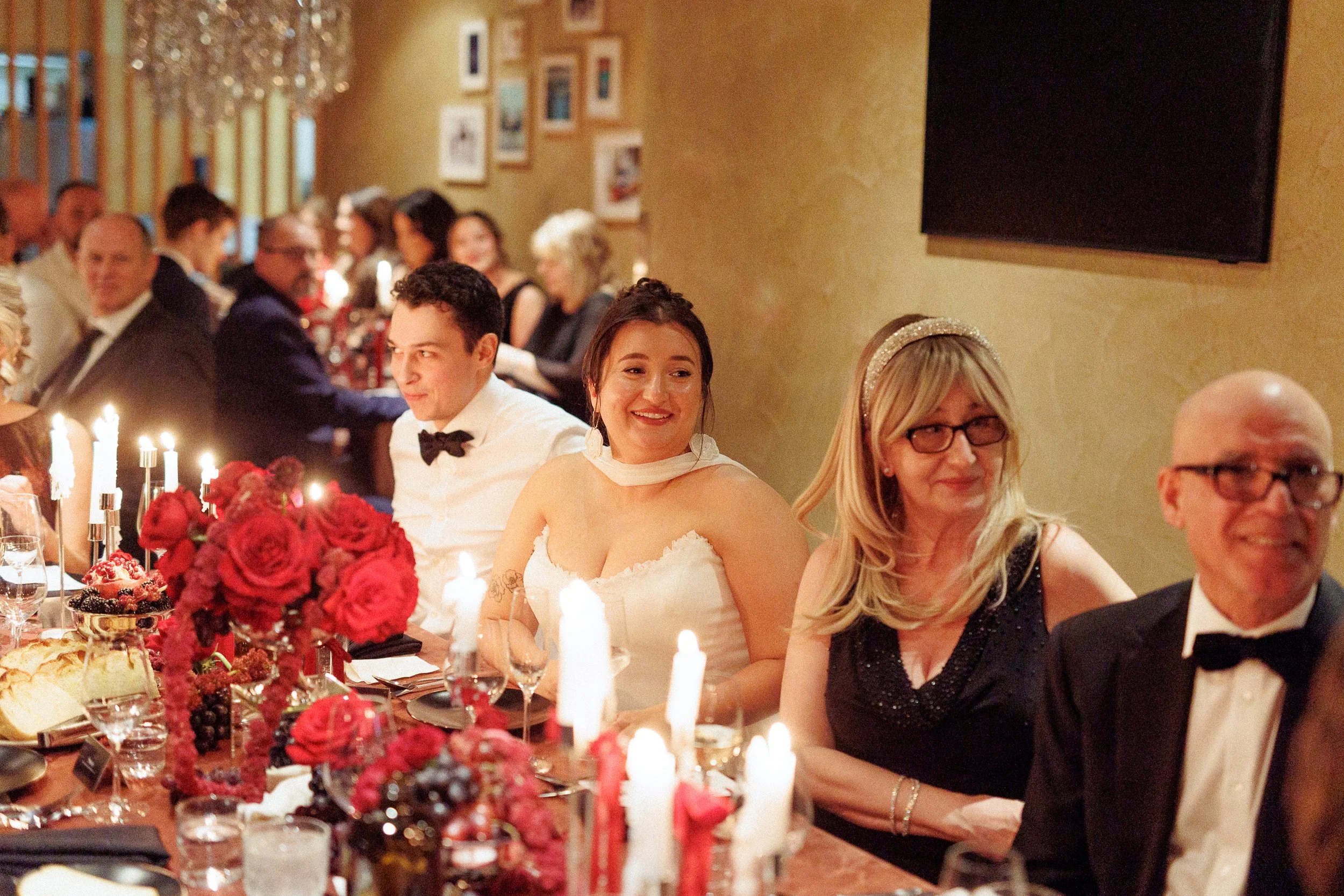 People dining at a formal event with a long table decorated with candles and flowers, in a warmly lit room.