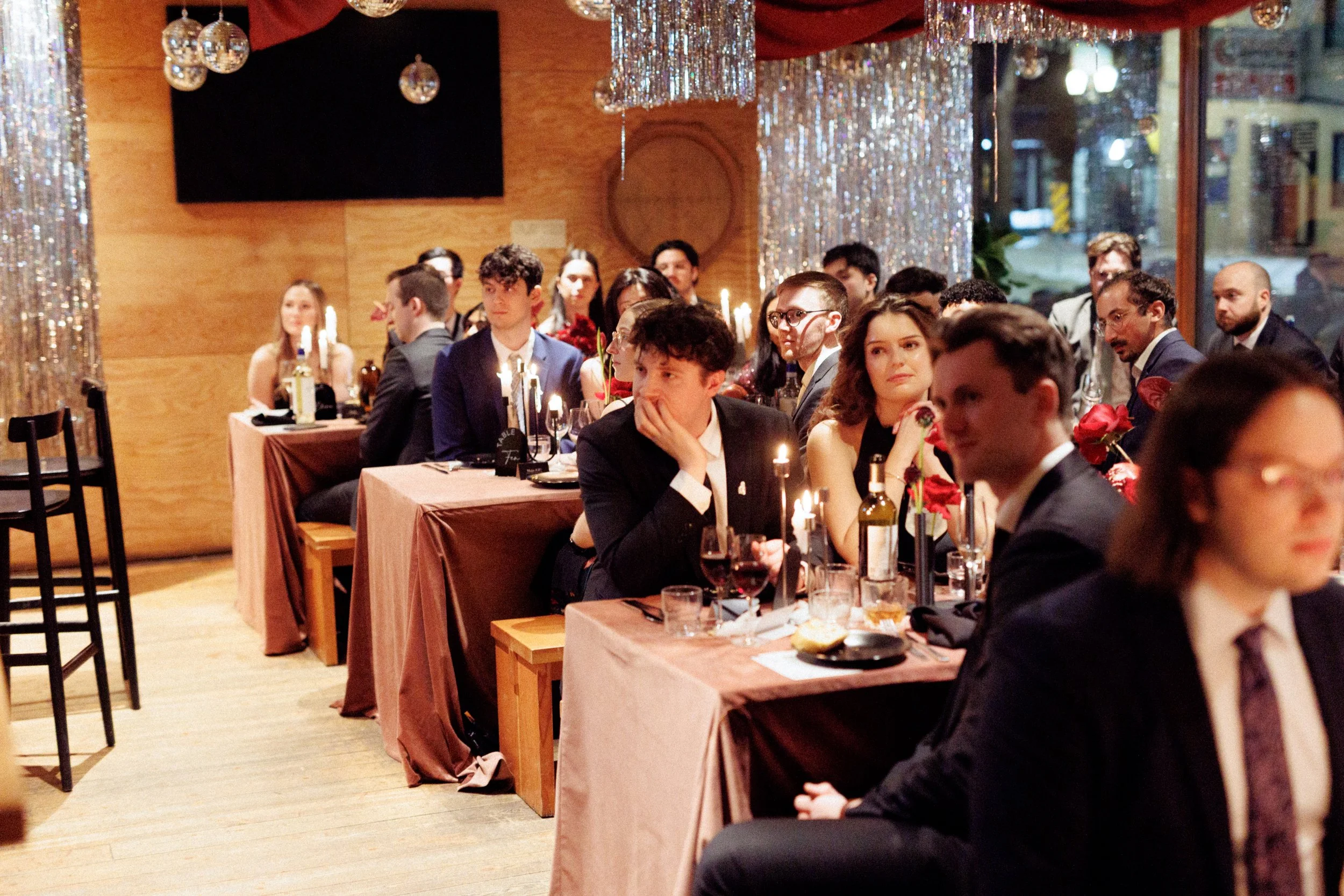 People sitting at tables during a formal dinner in a decorated venue with hanging disco balls, candles, and billowing red fabric