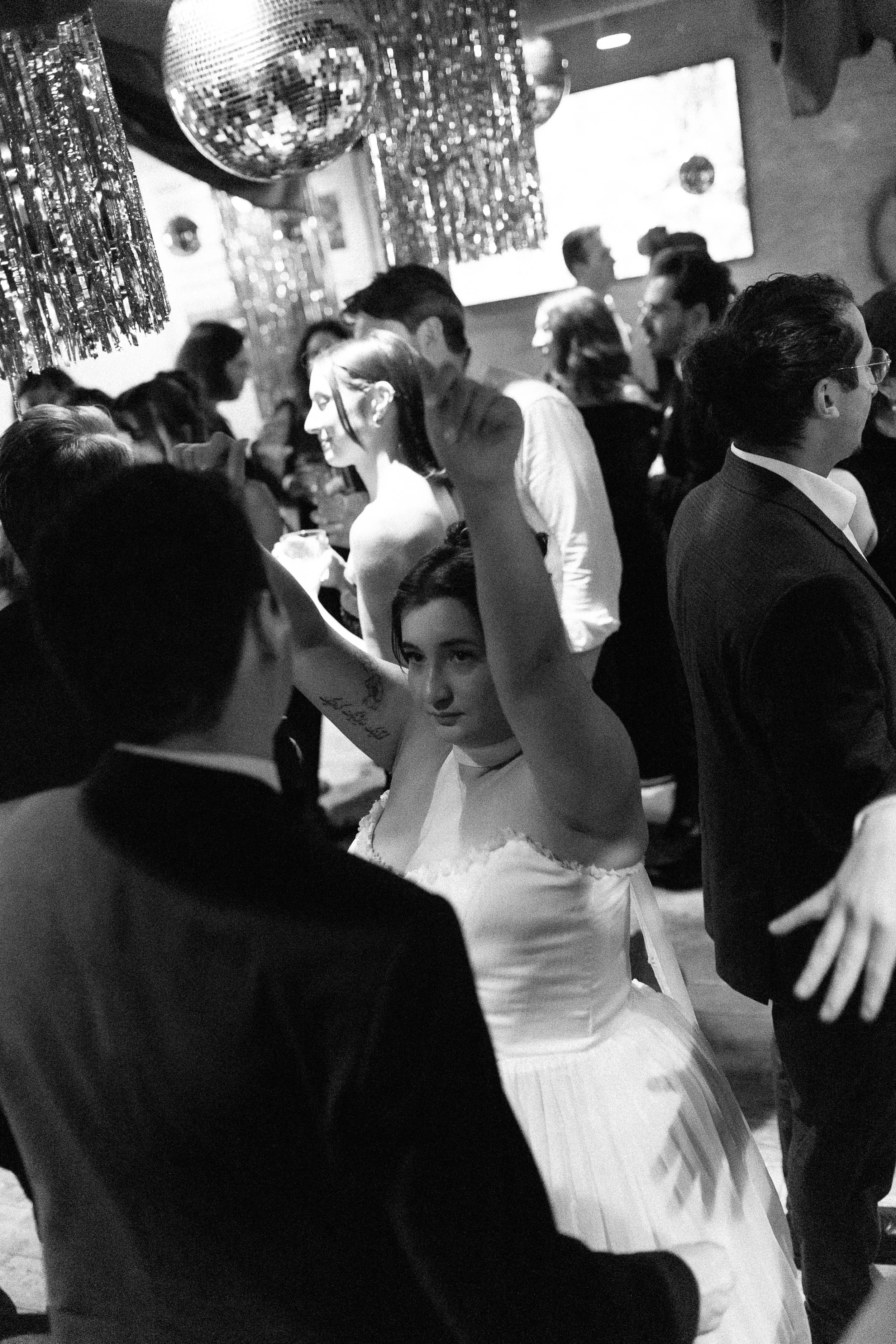 People dancing at a party or celebration, with disco balls and festive decorations hanging from the ceiling.