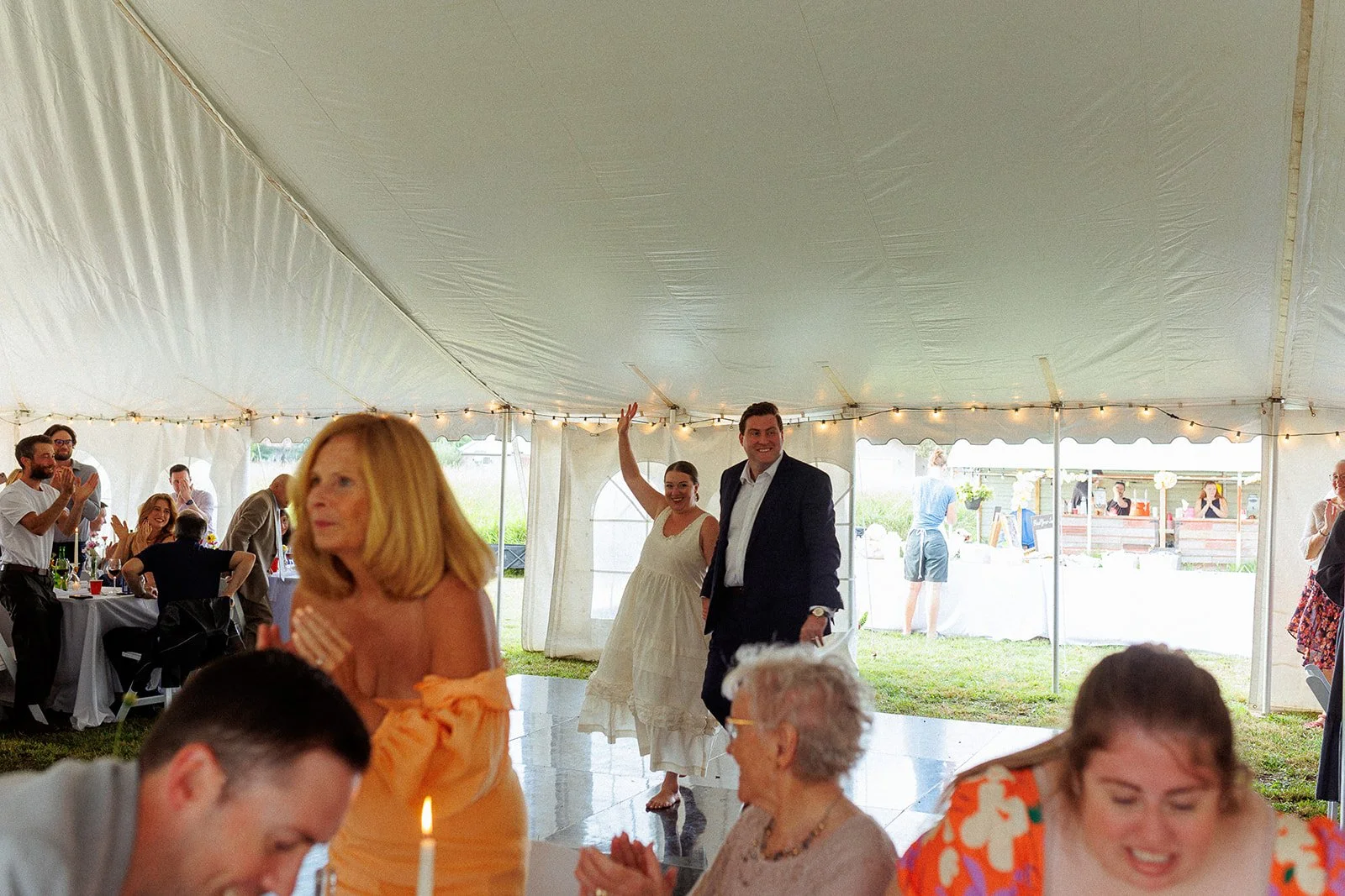 People dancing and celebrating at a wedding reception under a large tent with string lights.