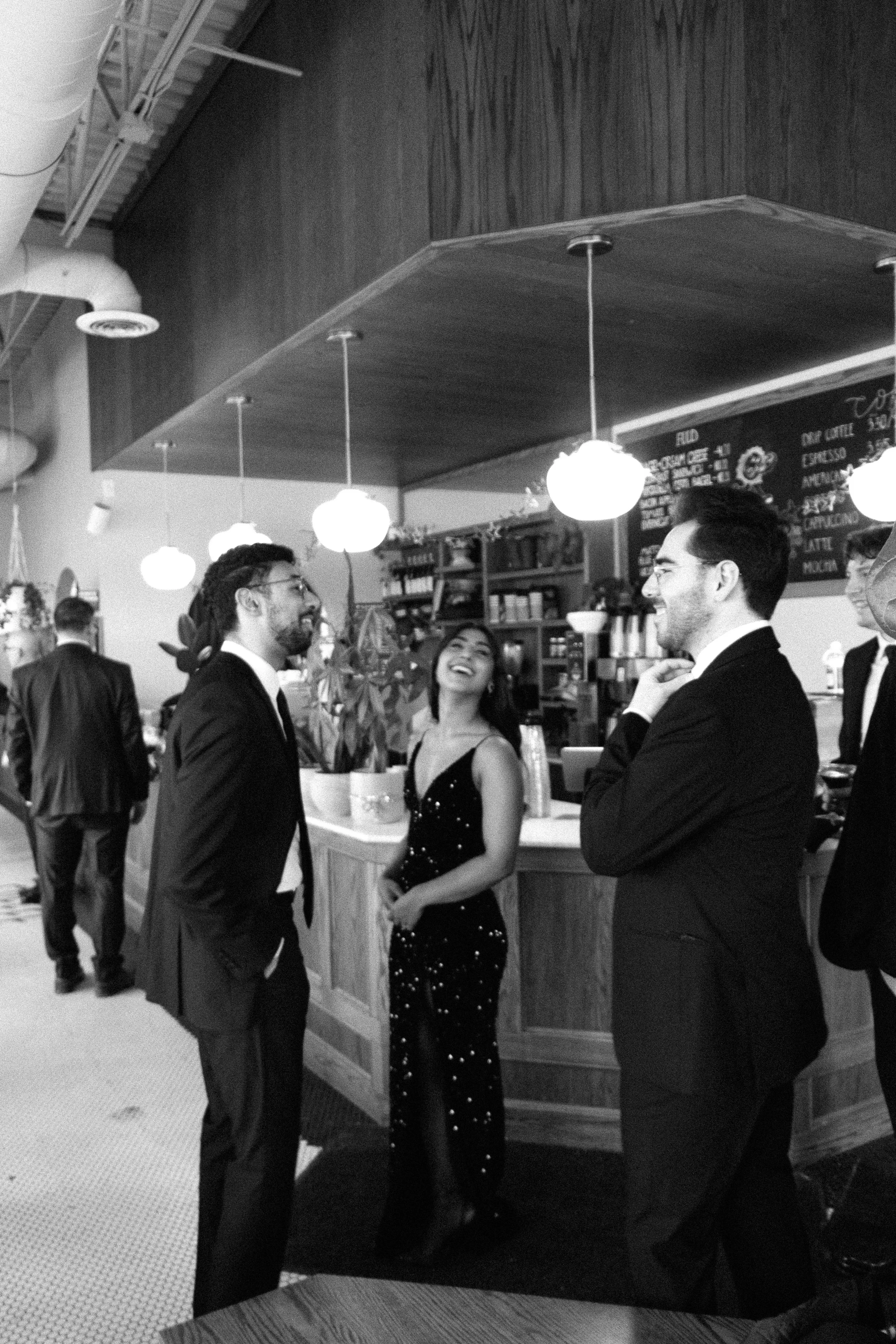 Group of people in tuxedos and evening dresses talking and laughing in a cafe or restaurant.

