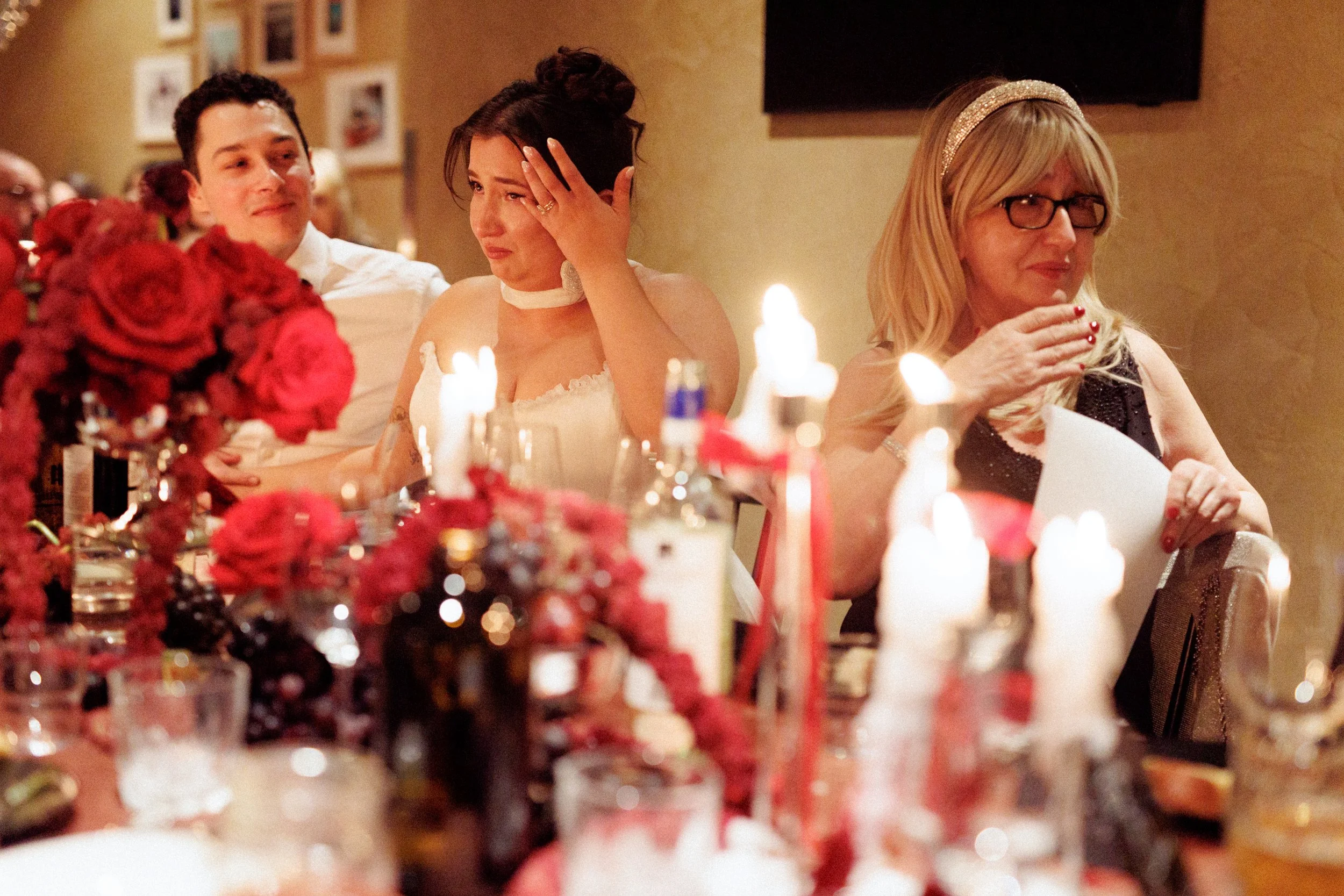People sitting at a table with candles and flowers, showing emotional reactions during a celebration or event.