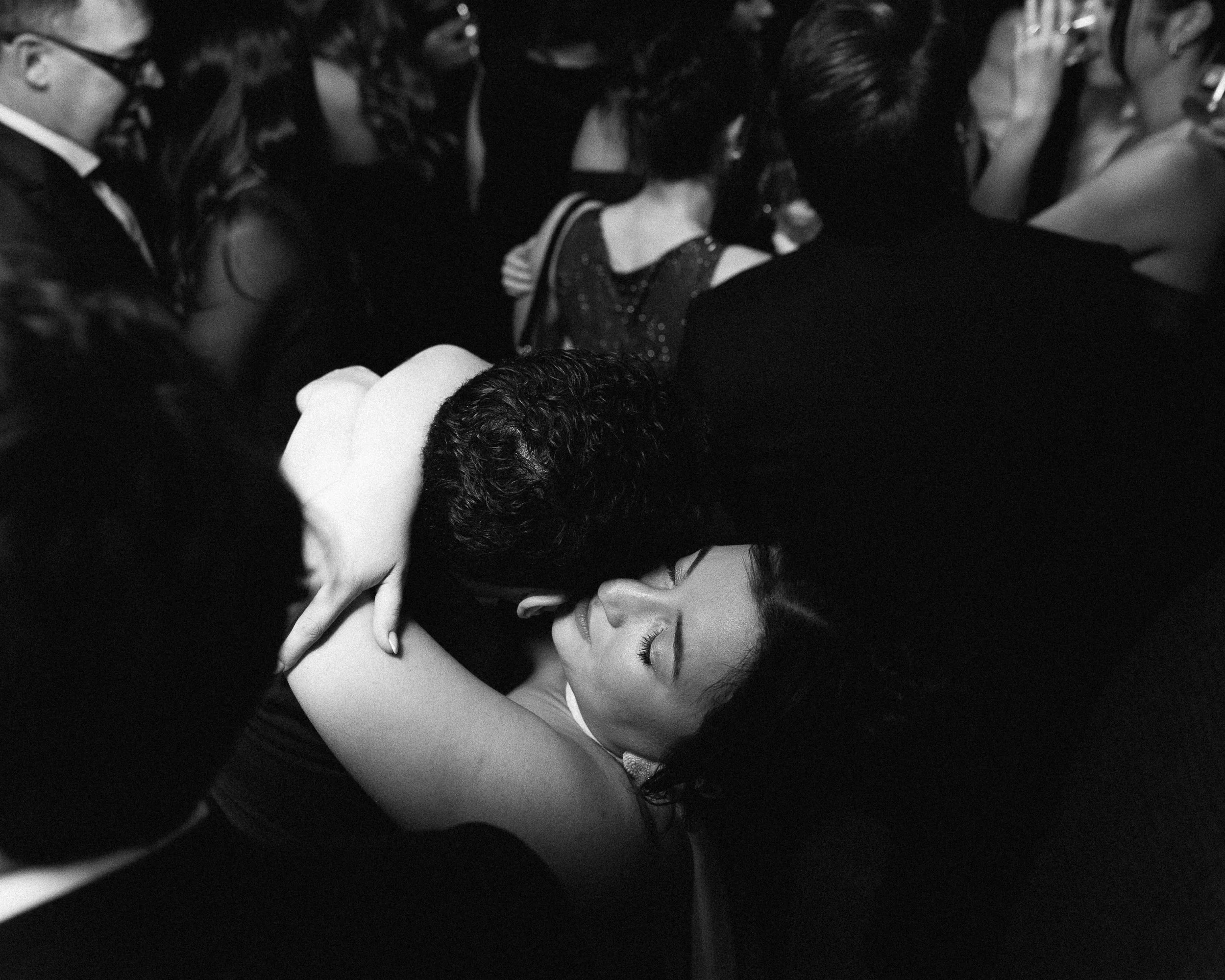 A woman is being kissed on the cheek by a man in a crowd at a formal event.