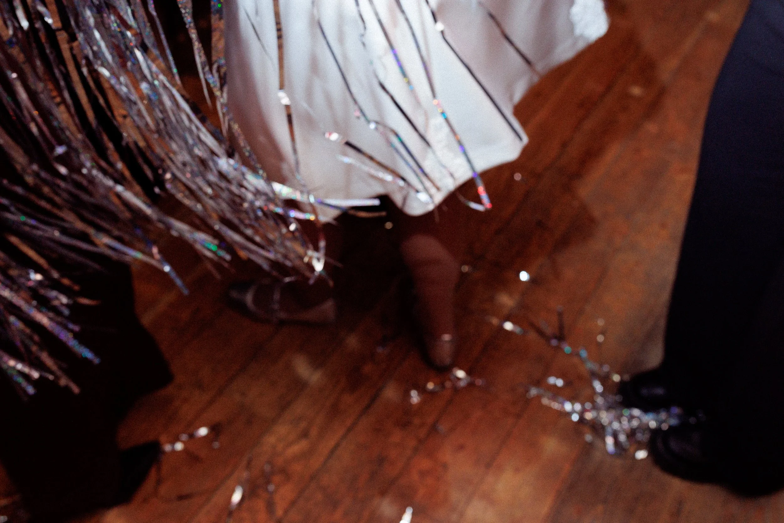 Close-up of festive decorations including tinsel and a white fabric with silver streamers on a wooden floor.