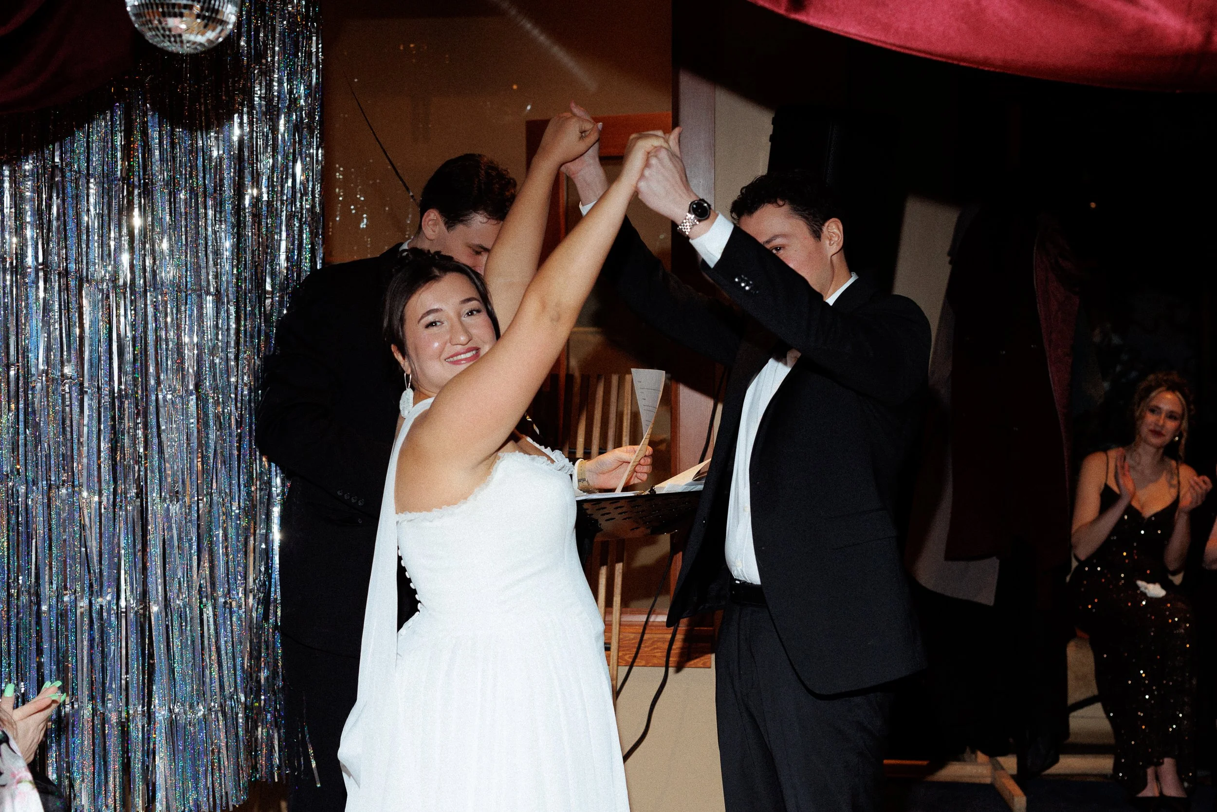A bride and groom dancing at their wedding reception with guests clapping in the background.