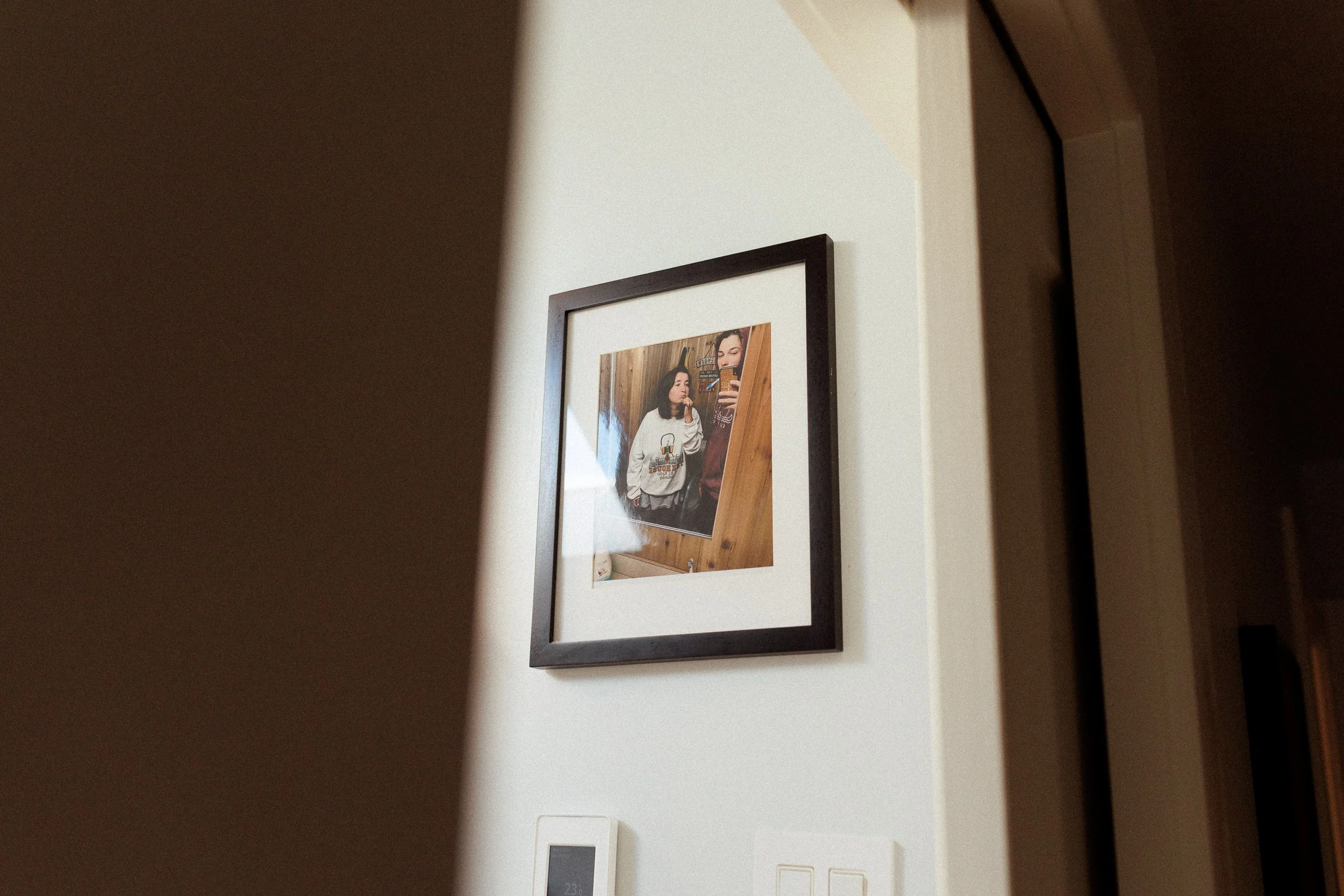 Framed mirror image of two women, one in a white sweater and one in brown, with wood paneling background.