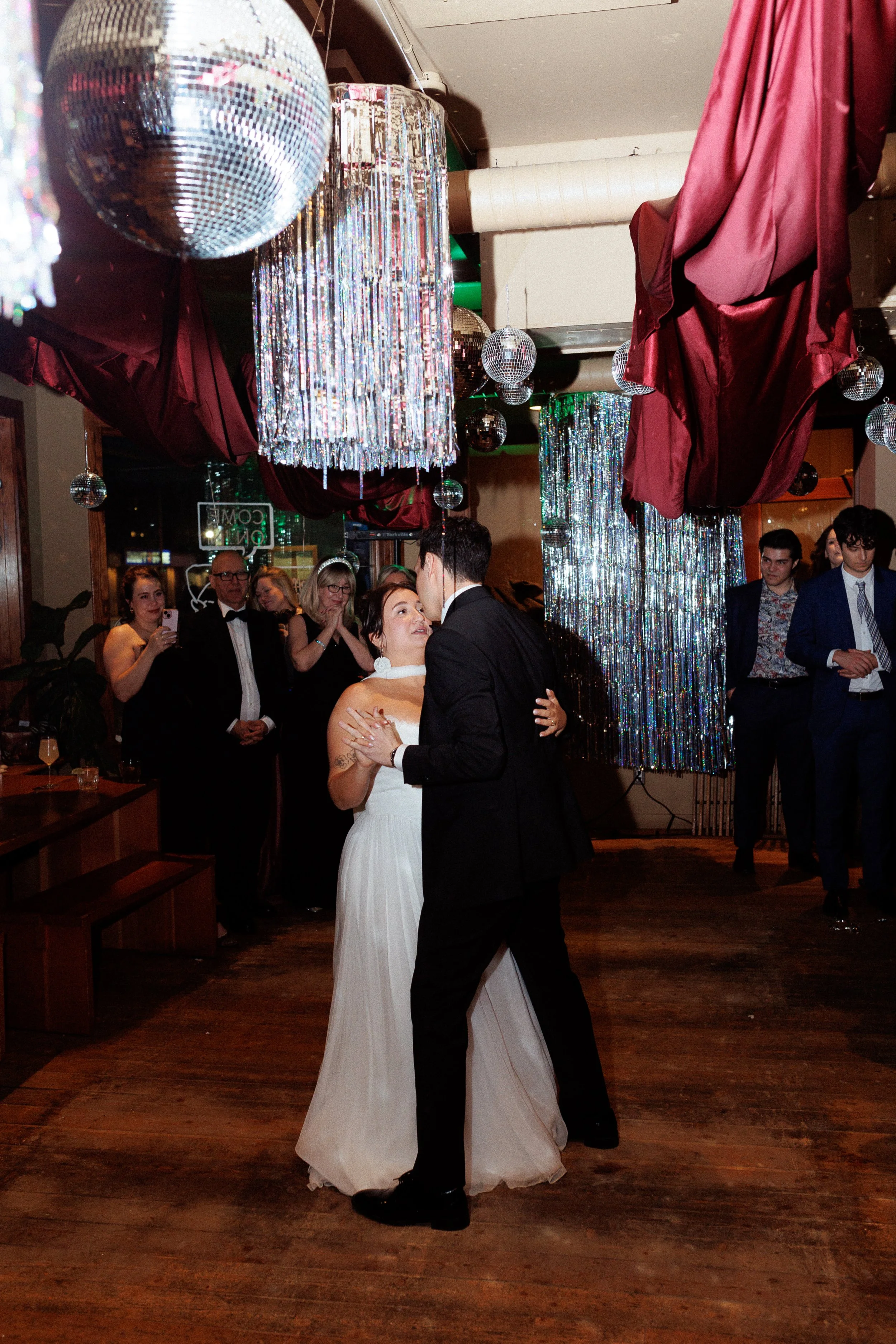 Couple dancing at a wedding reception, surrounded by guests and party decorations.