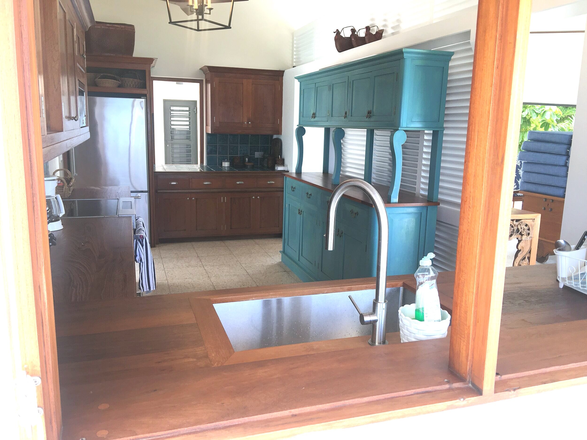This kitchen built in 1996 for a St. Martin beach house occupies the narrrow end of a large room and is separated by a slatted screen wall . Again the painted free- standing credenza provides variety and colour. The old fixed louvred window opening