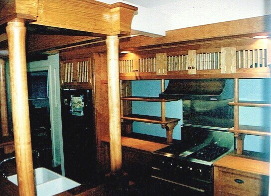 This small kitchen on Cape Cod shows a grand canopied Island with teak counter and farmhouse sink. The cabinetwork in Cherry uses spindled doors to provide well ventilated storage. Brackets and turned columns supprt open shelving either side of the