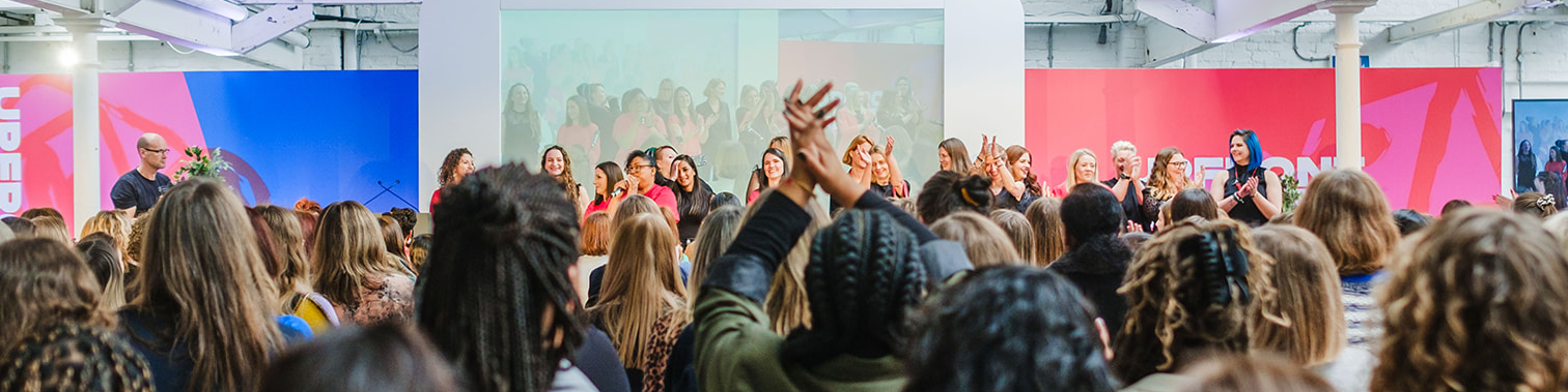 Women at the UPFRONT conference on their feet clapping and celebrating each other