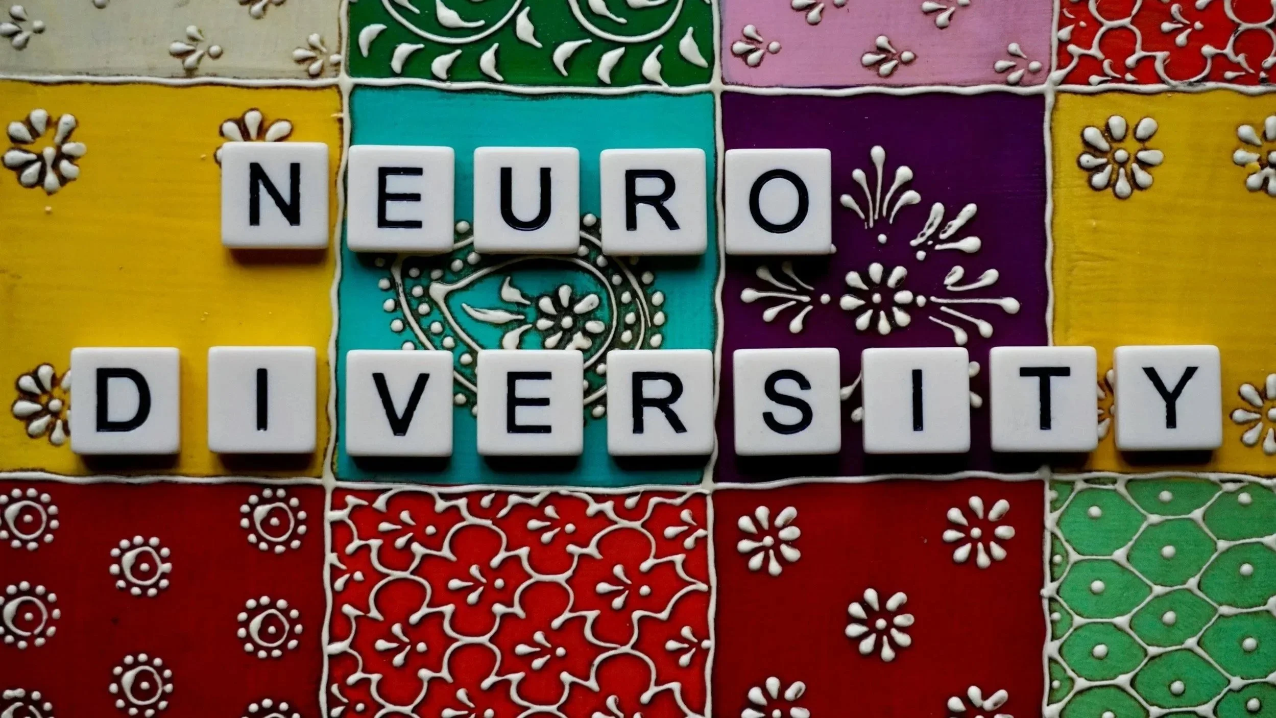 Colorful decorated tiles with the words "NEURO DIVERSITY" spelled out in white lettered blocks.