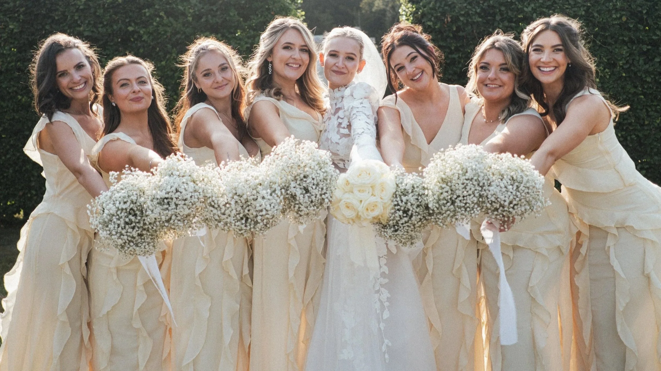Bride and seven bridesmaids smiling and holding bouquets of white flowers made by Wed & Prosper. lemon bridesmaid dresses, isle of wight wedding