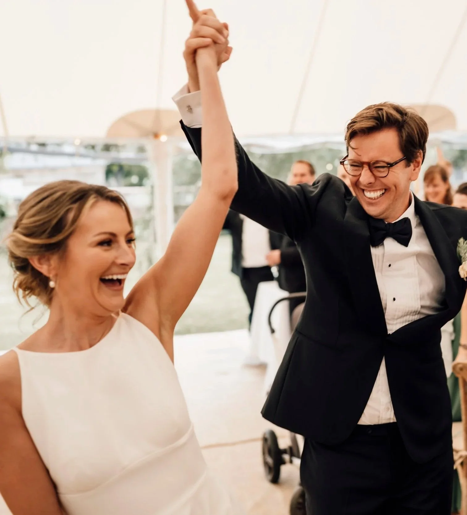 A bride and groom happily dancing at their wedding reception, holding hands in the air, smiling and enjoying the moment.