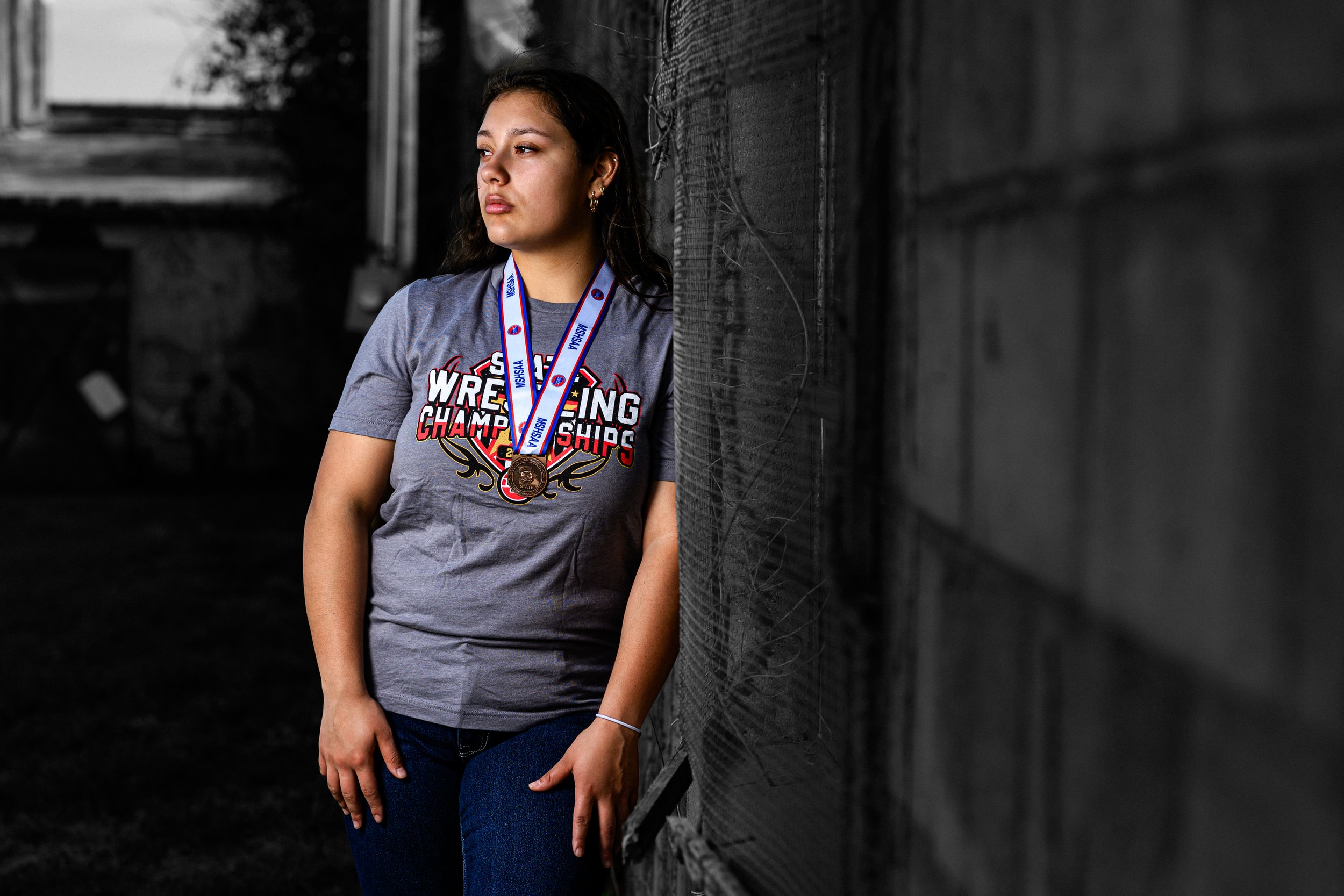 Person wearing a gray wrestling championships t-shirt and medal, standing against a wall.