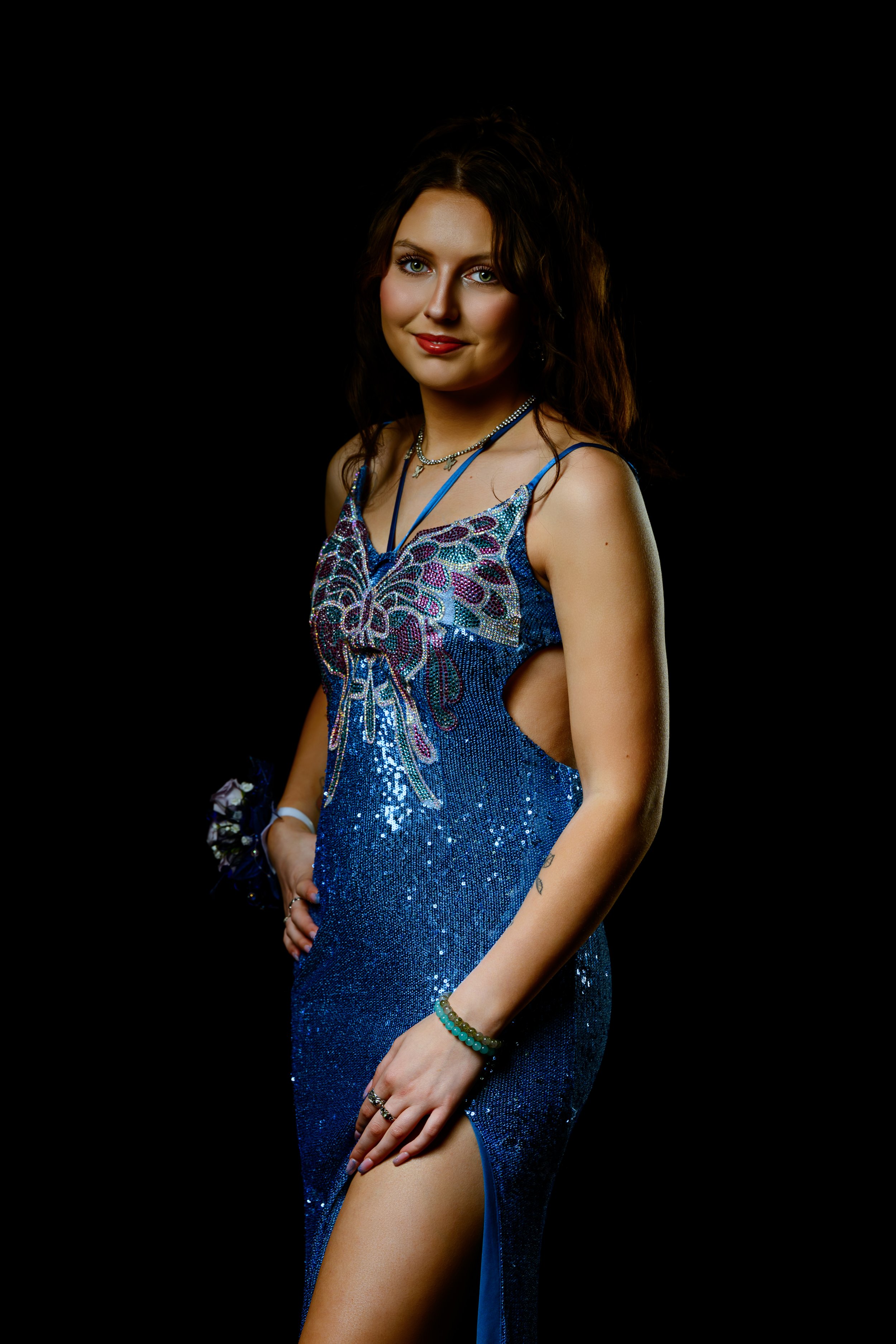 Woman in a blue sequined gown with butterfly pattern, posing against a black background.