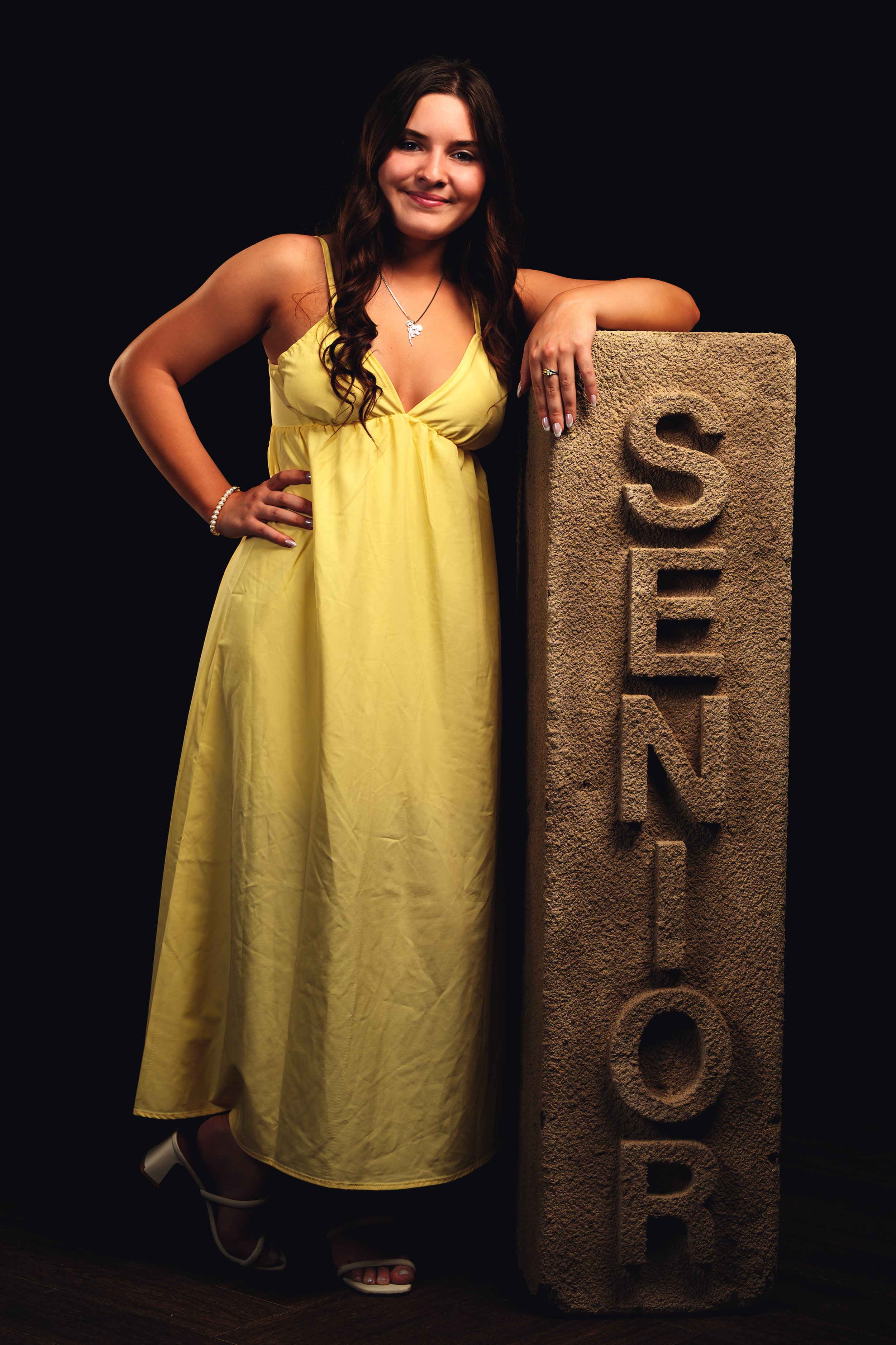 Person in a yellow dress standing next to a pillar with the word 'SENIOR' carved on it.
