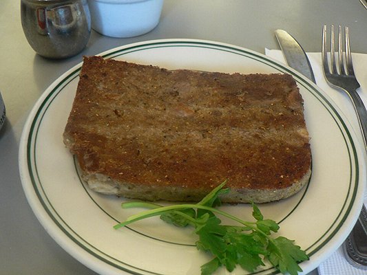A slice of fried scrapple served on a plate with a sprig of parsley