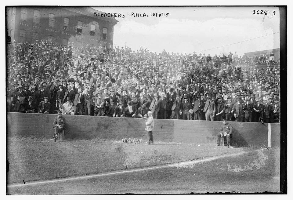 B&W photo of men occupying uncovered seats at the far end of a baseball field