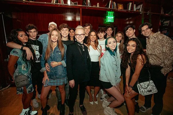A young man dressed in black surrounded posing with a bevy of other youthful people